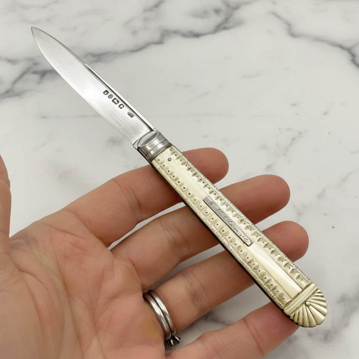 Hand holding a decorative folding knife on a marble surface