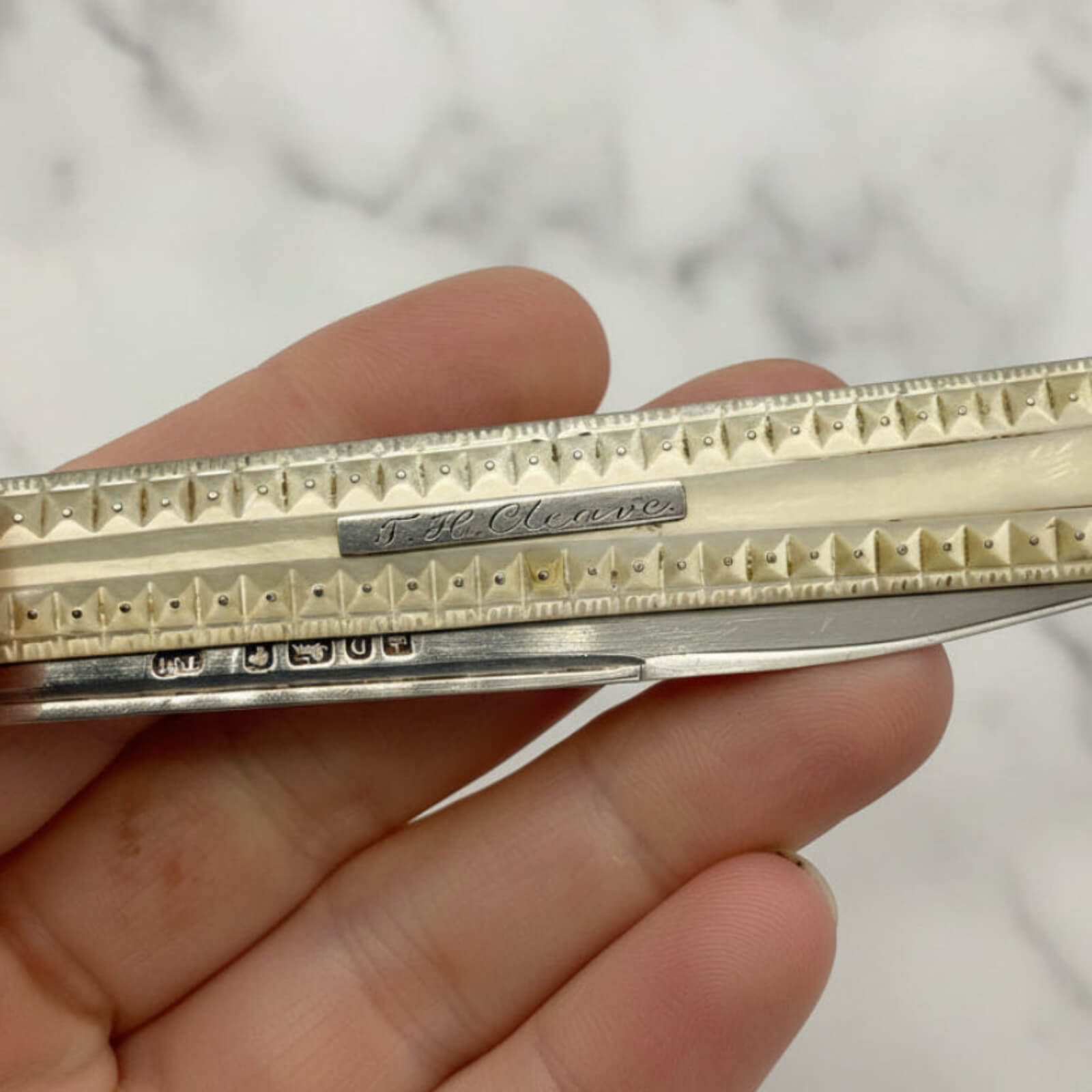 Silver pocket knife held in a hand with a blurred background