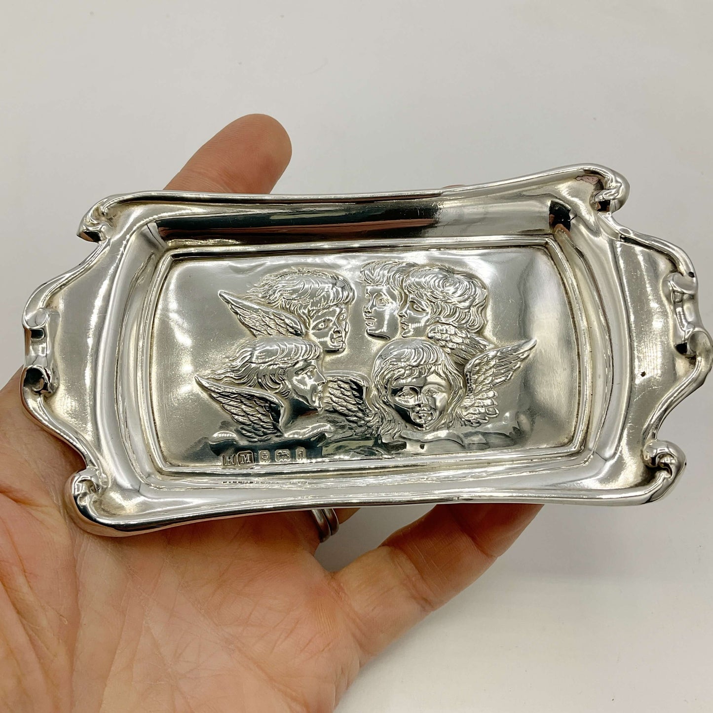 Silver tray with engraved designs held by a hand against a white background