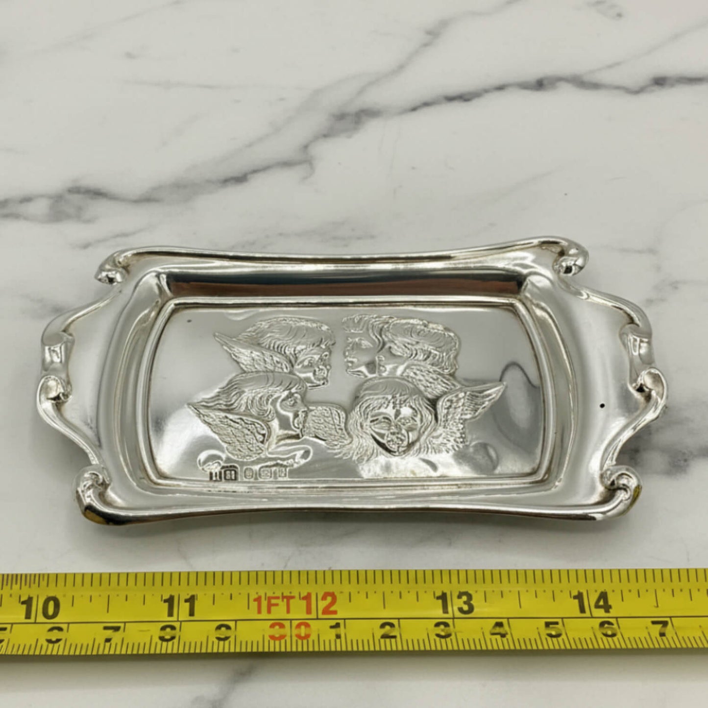 Silver tray with engraved design on a marble surface with a measuring tape for scale.