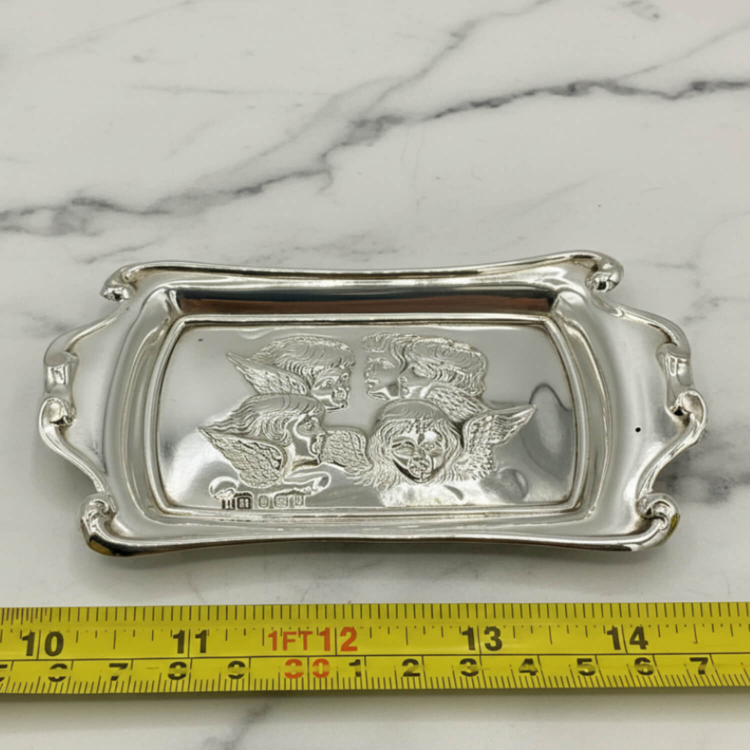 Silver tray with engraved design on a marble surface with a measuring tape for scale.