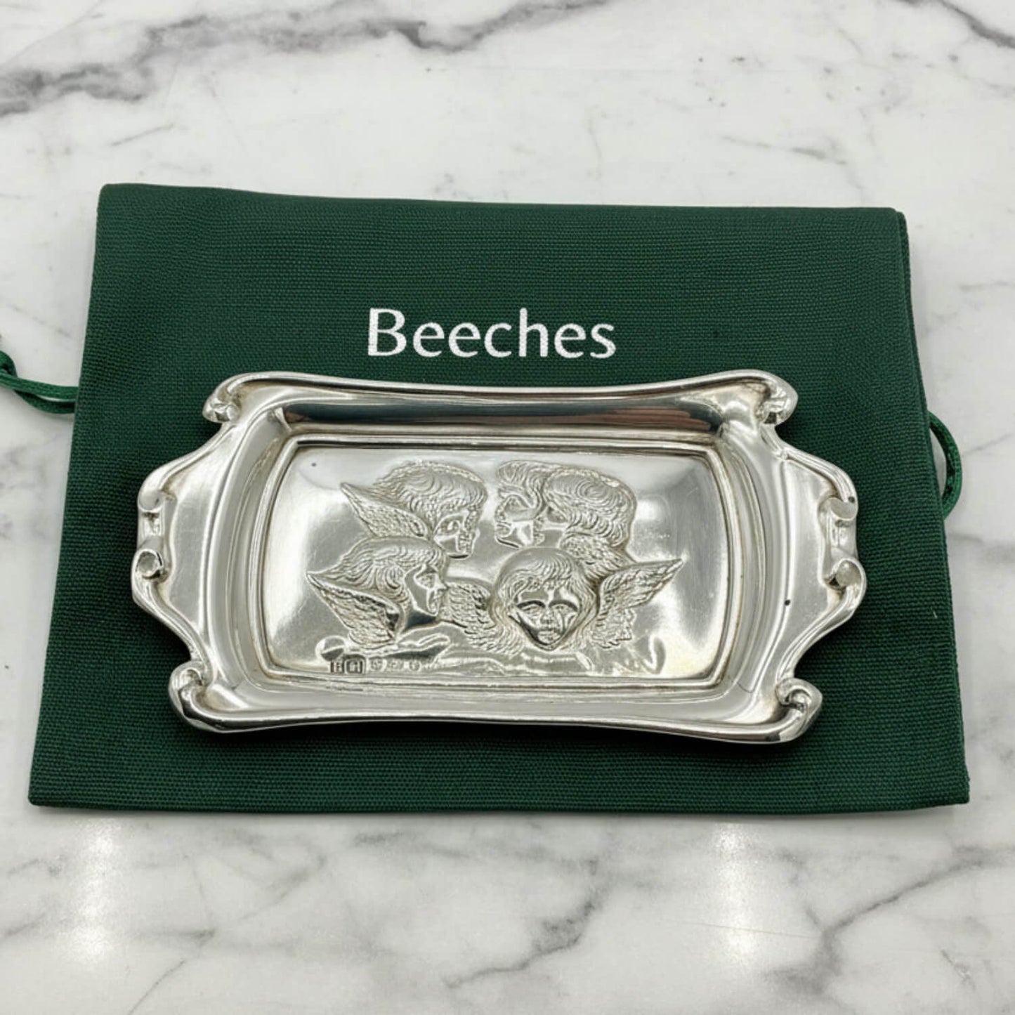 Silver decorative tray with intricate designs on a green cloth labeled 'Beeches Vintage' on a marble background.