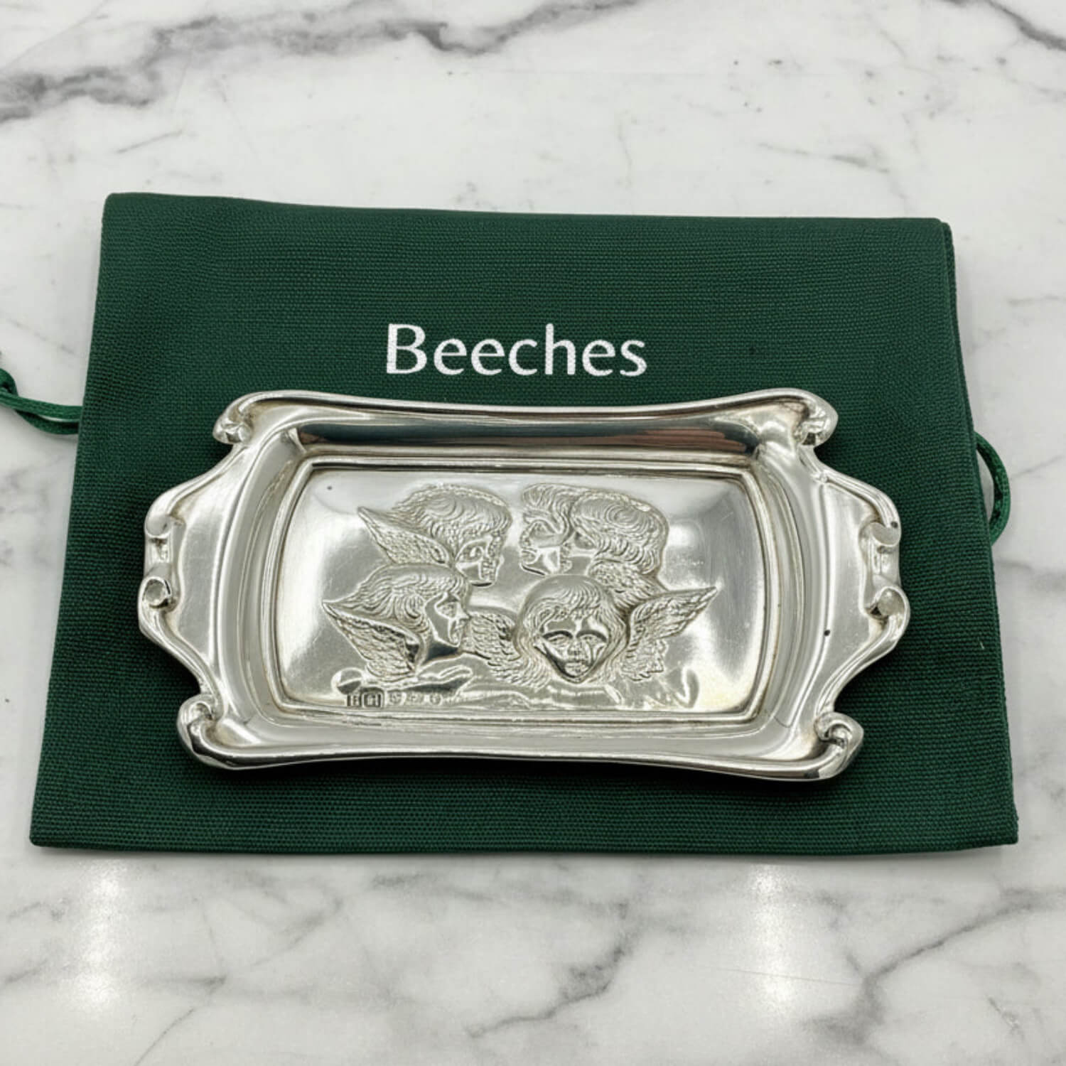 Silver decorative tray with intricate designs on a green cloth labeled 'Beeches Vintage' on a marble background.
