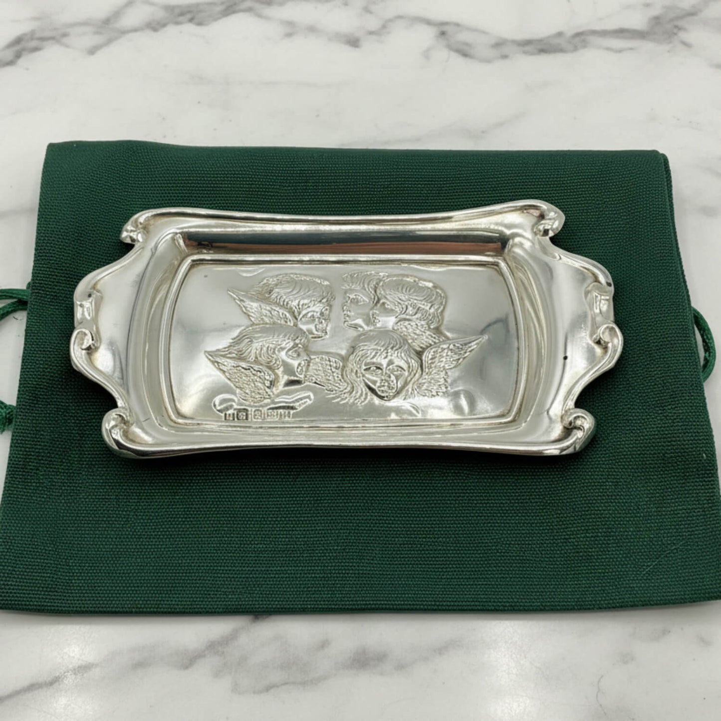 Silver tray with engraved designs on a green cloth bag