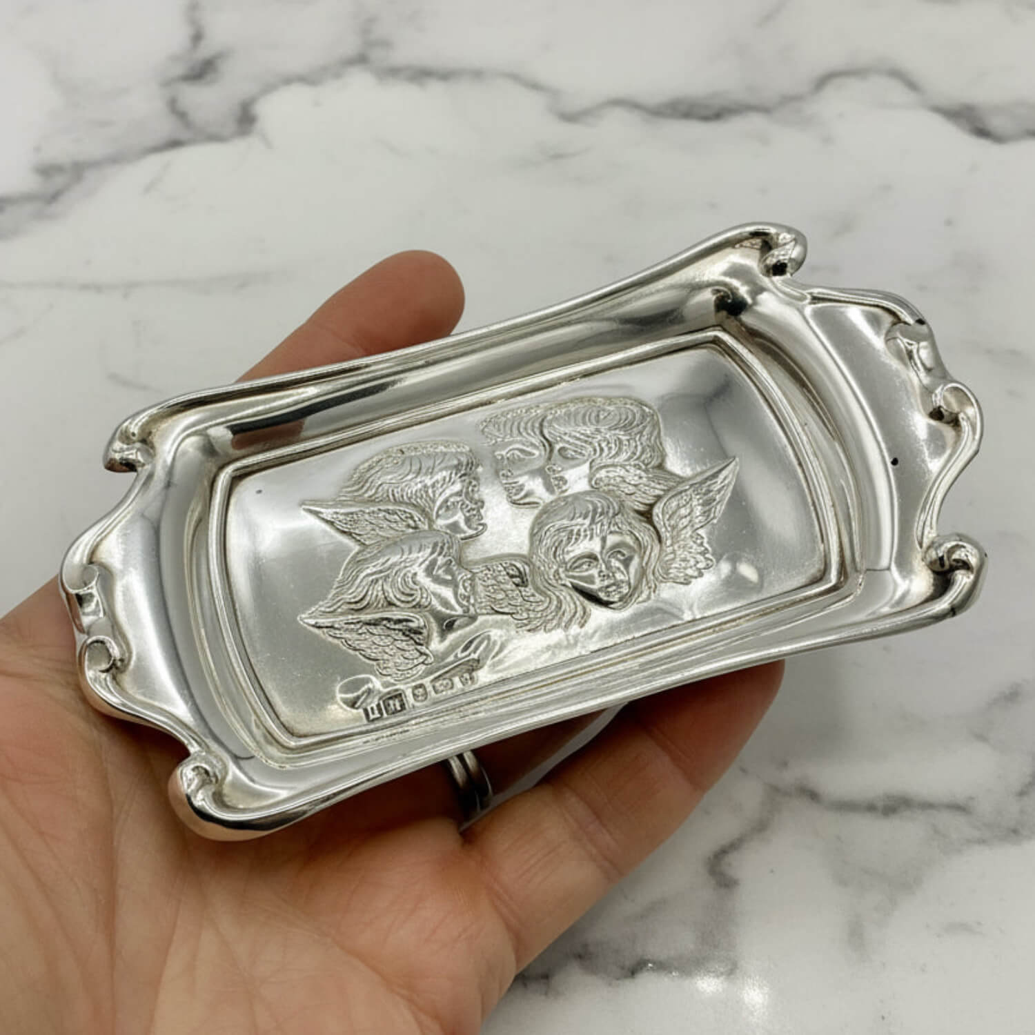 Silver decorative tray with a cherub design in a hand against a marble background