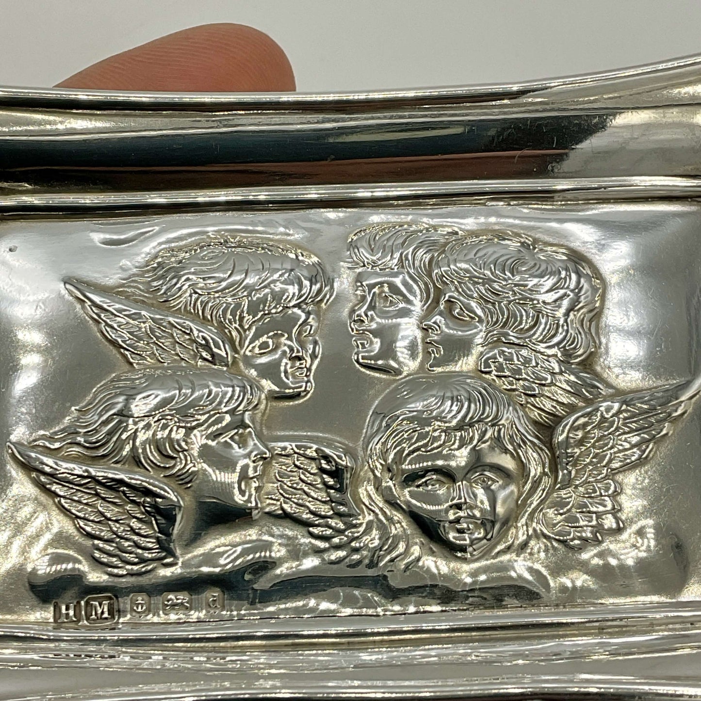Silver dish with cherub faces and wings embossed on a white background