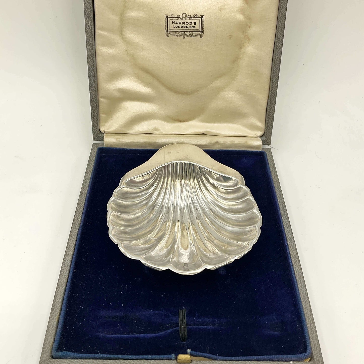 Silver shell-shaped dish in an open jewelry box with 'Harrods' branding.