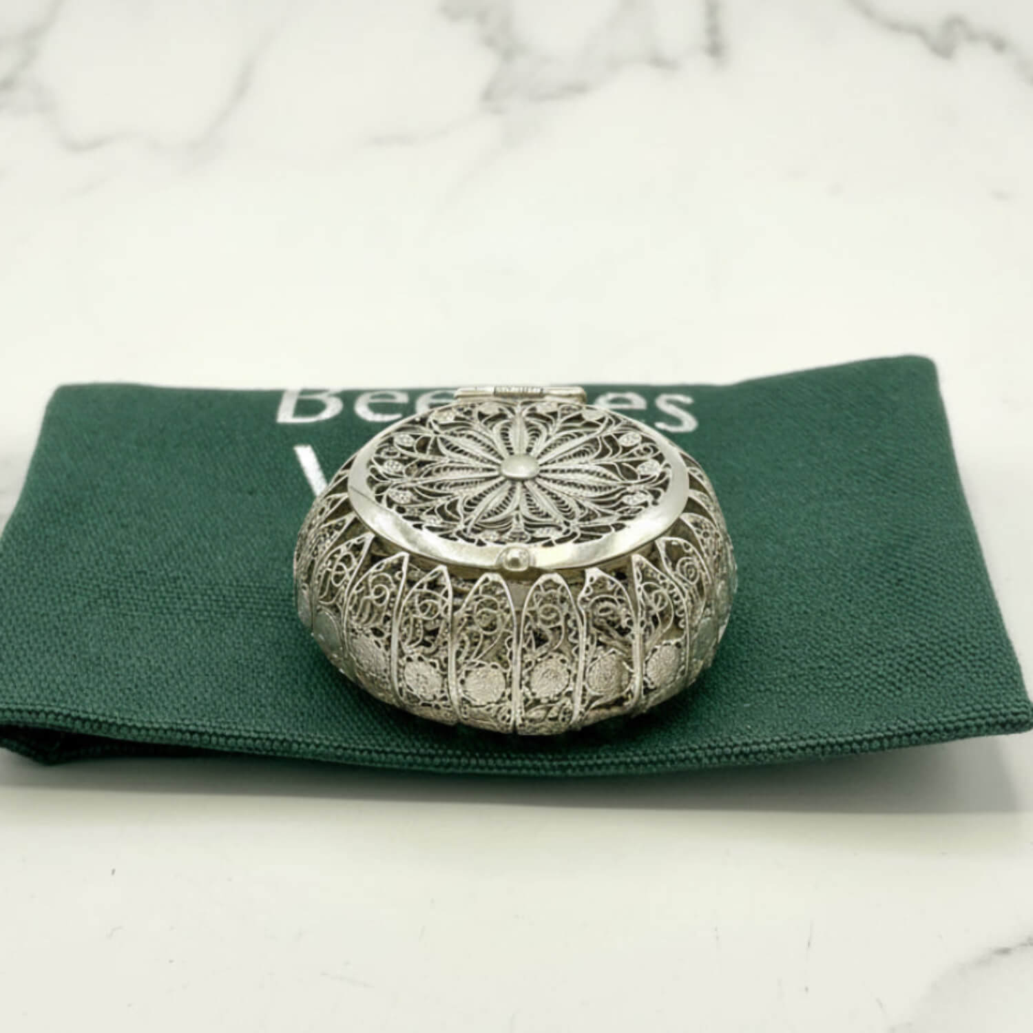 Decorative silver metal box on a green fabric with 'Beeches' text