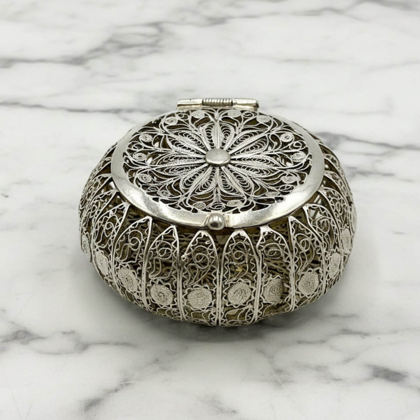 Decorative silver round box with intricate patterns on a marble surface
