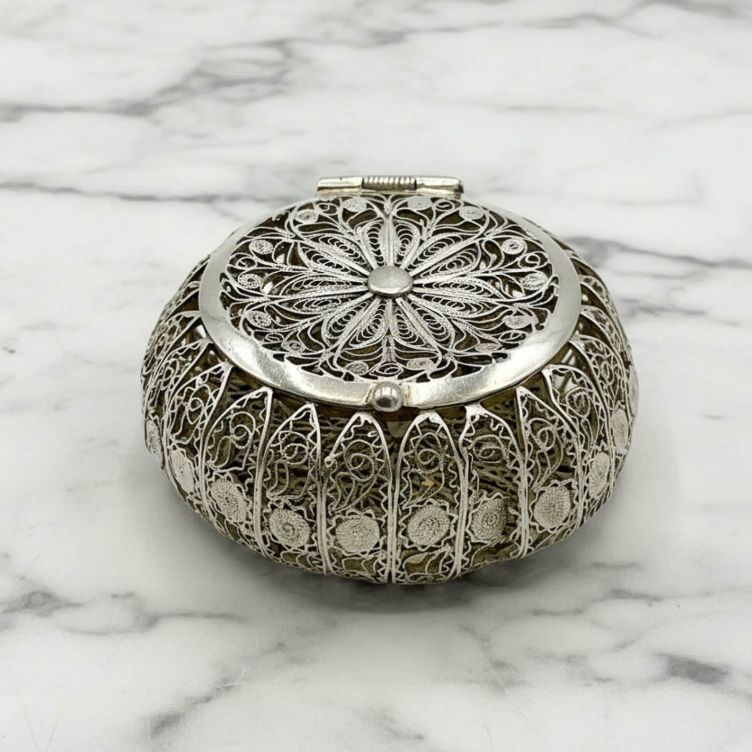 Decorative silver round box with intricate patterns on a marble surface