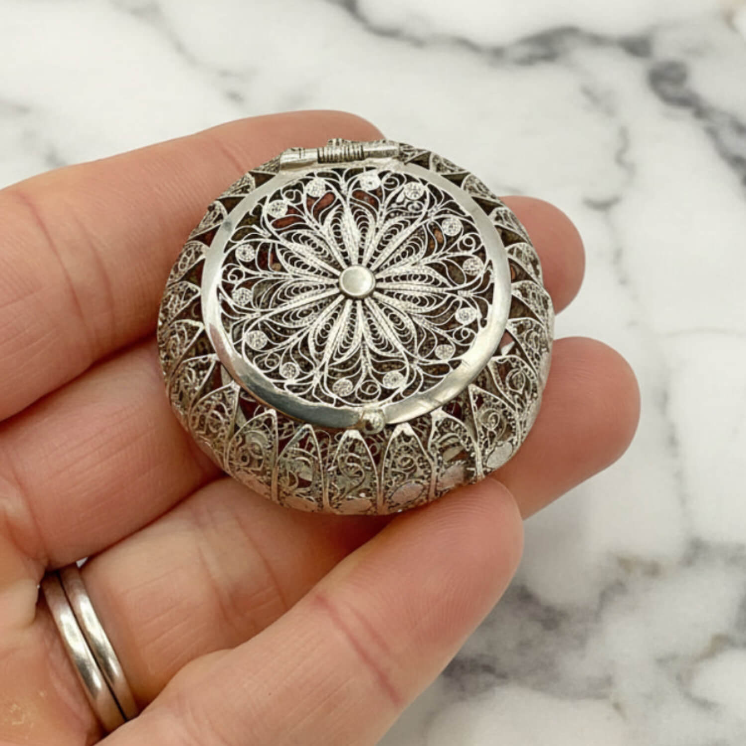 Antique Silver Filigree Box held in a hand against a marble background