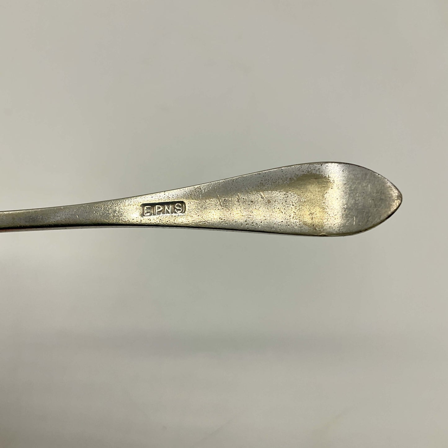 Close-up of a silver spoon with 'E.P.N.S.' engraving on a gray background
