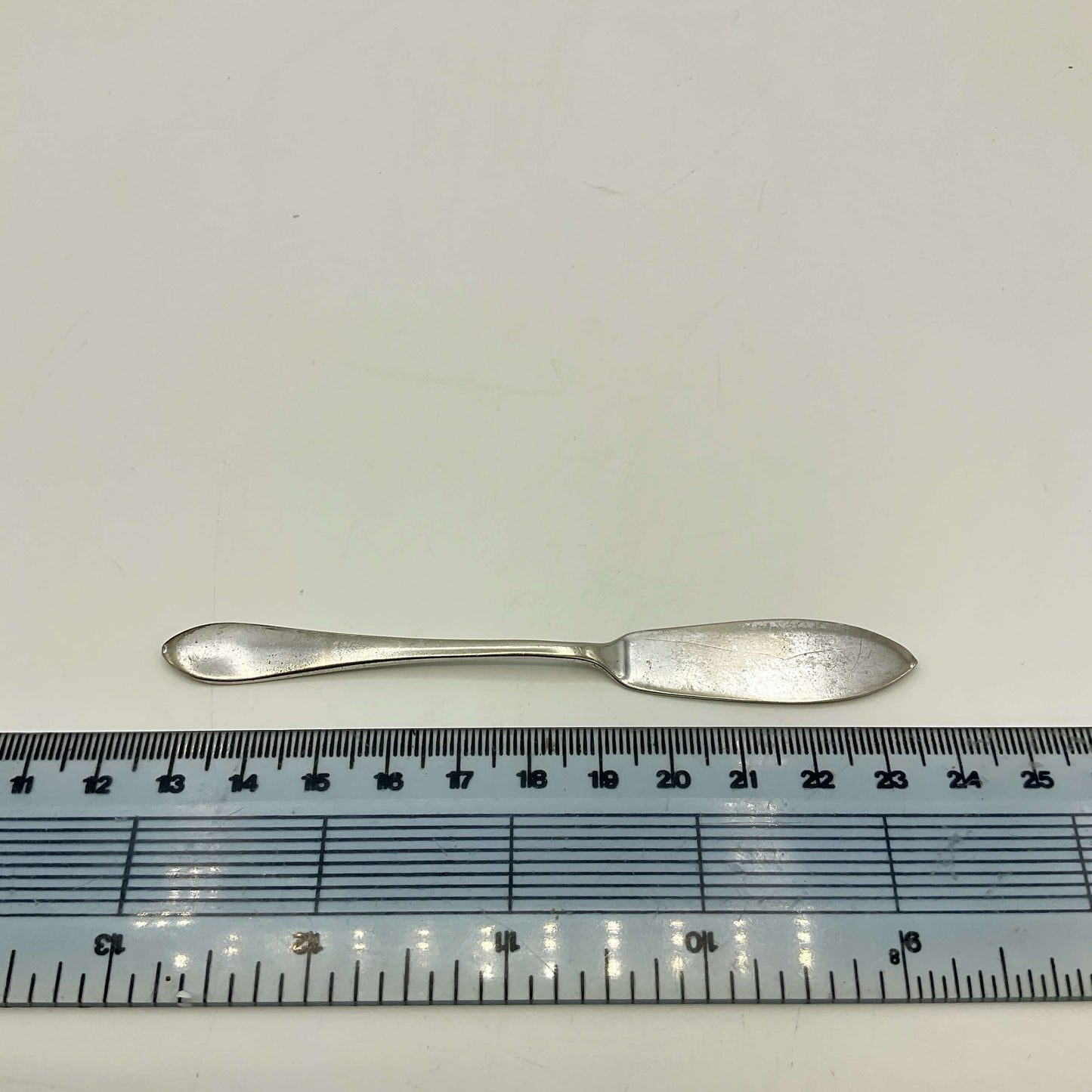 Silver plated butter knife next to a ruler on a white background