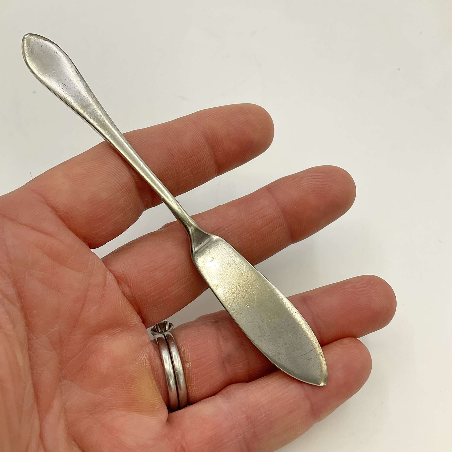 Silver plated butter knife held in a hand with a plain background