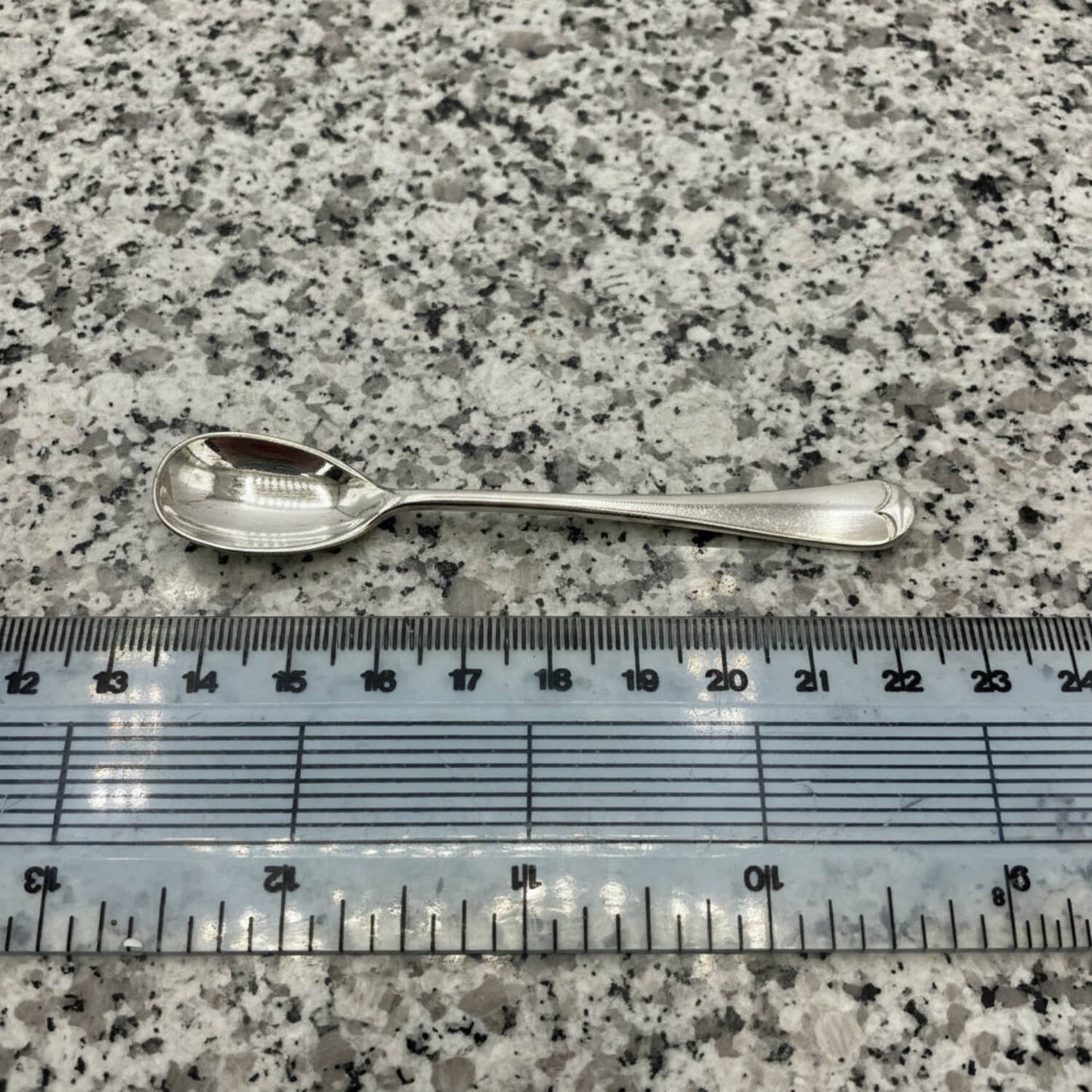 Silver spoon next to a ruler on a speckled surface