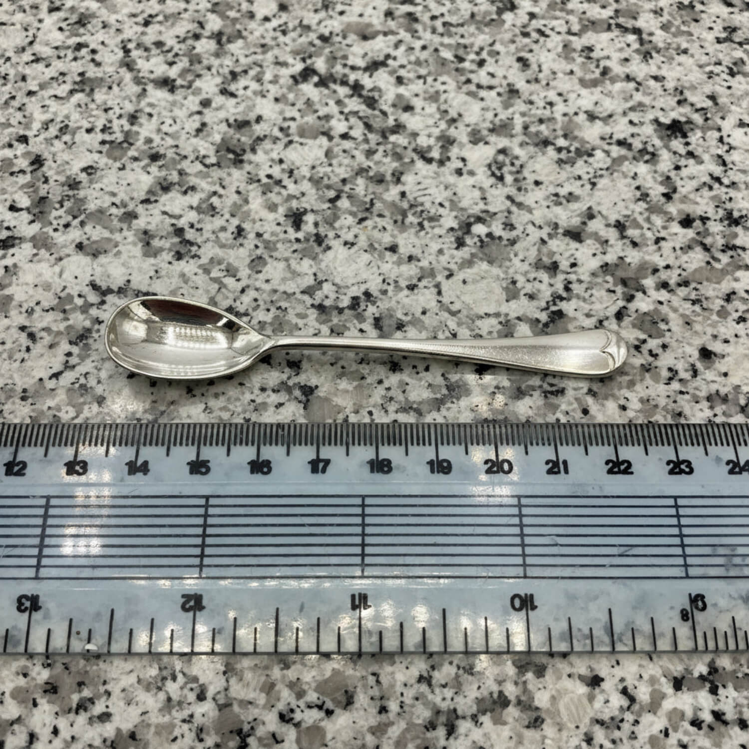 Silver spoon next to a ruler on a speckled surface