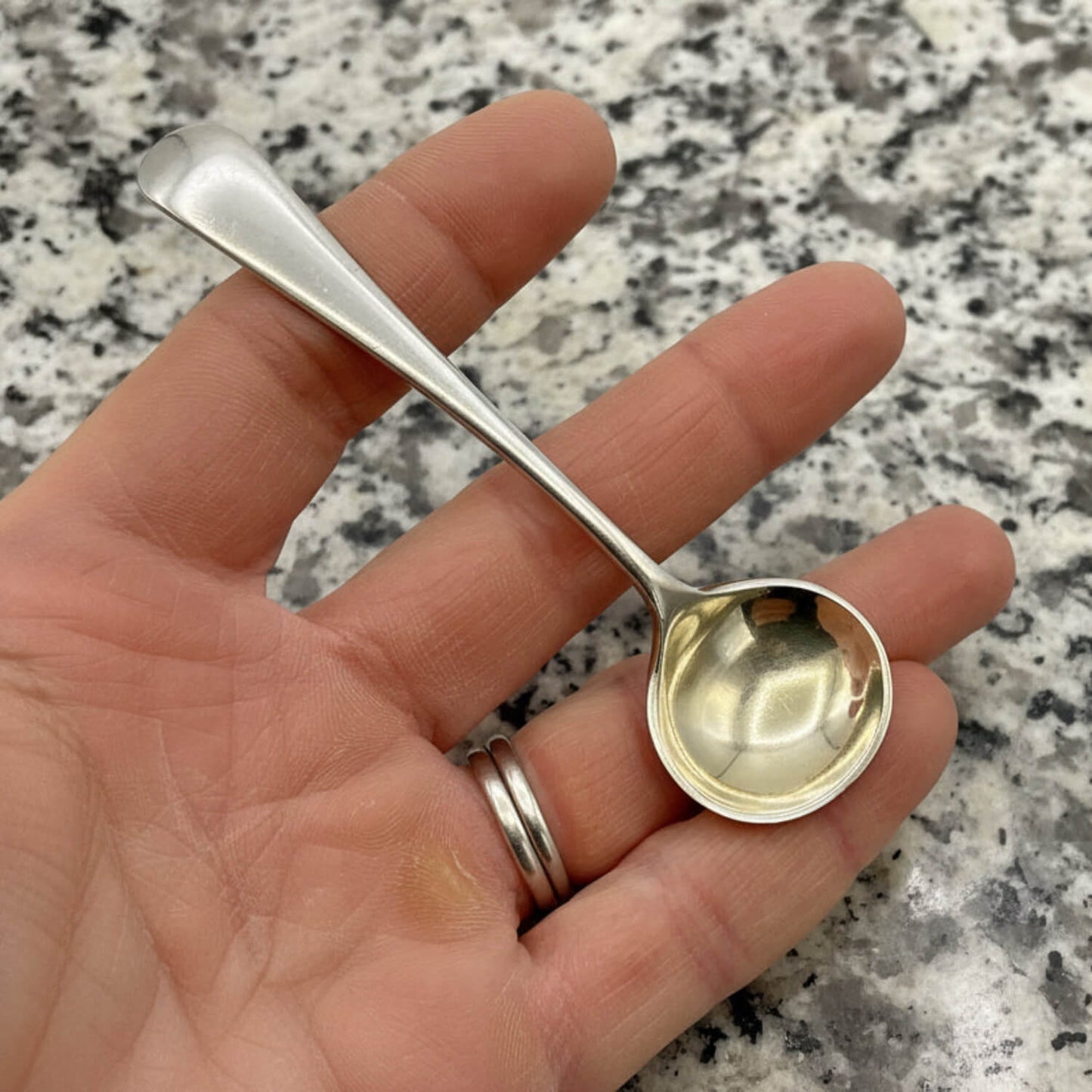 Small silver spoon held in a hand against a granite countertop background