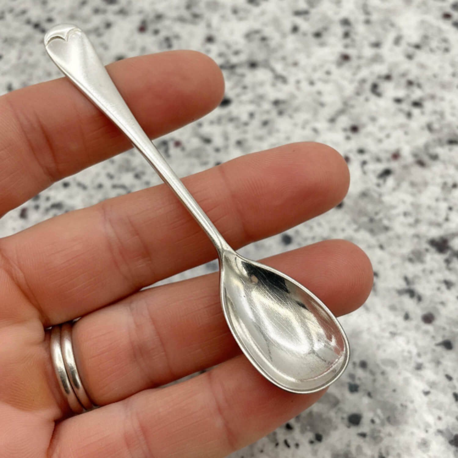 Silver spoon held between fingers against a speckled grey background