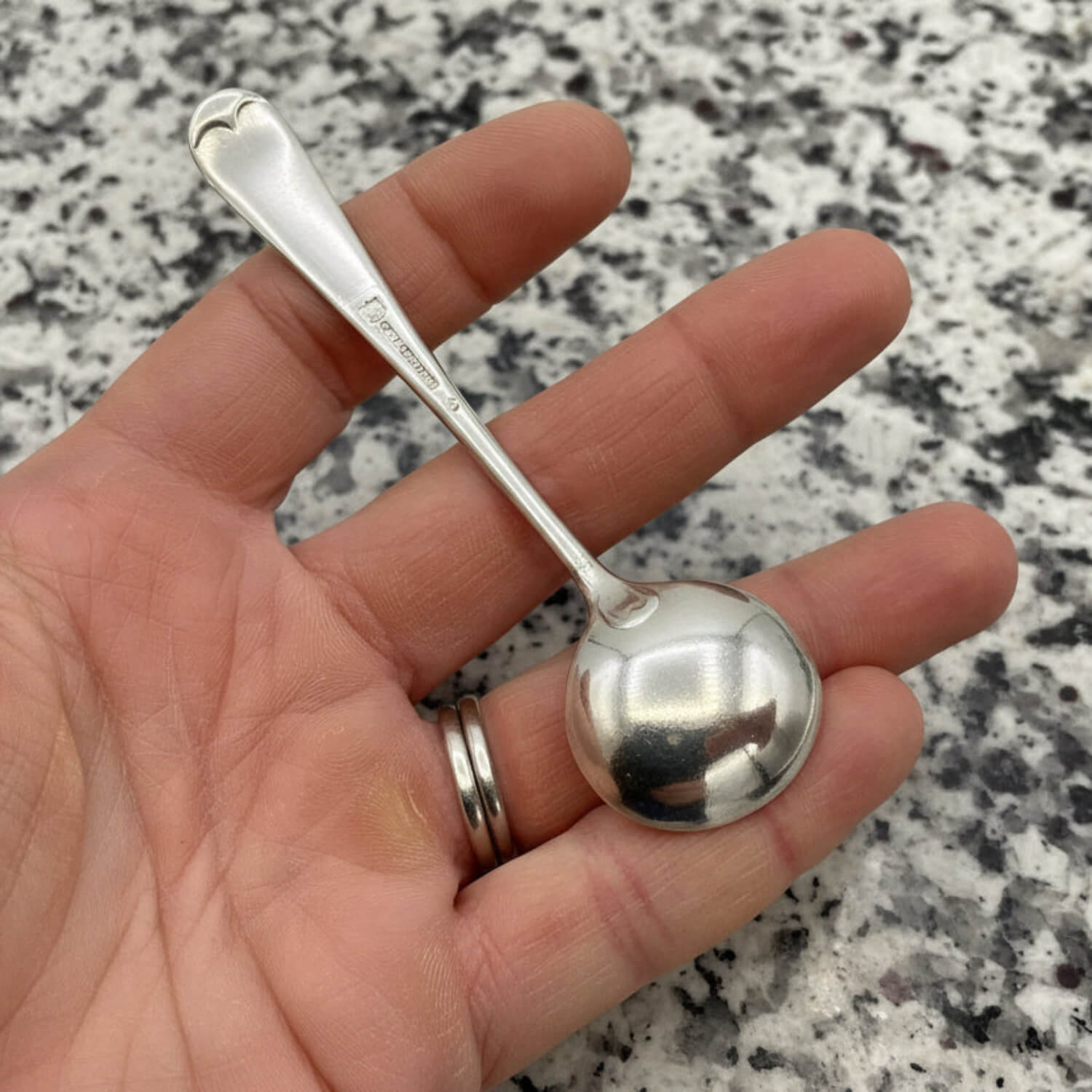 Silver spoon held in a hand against a marble countertop