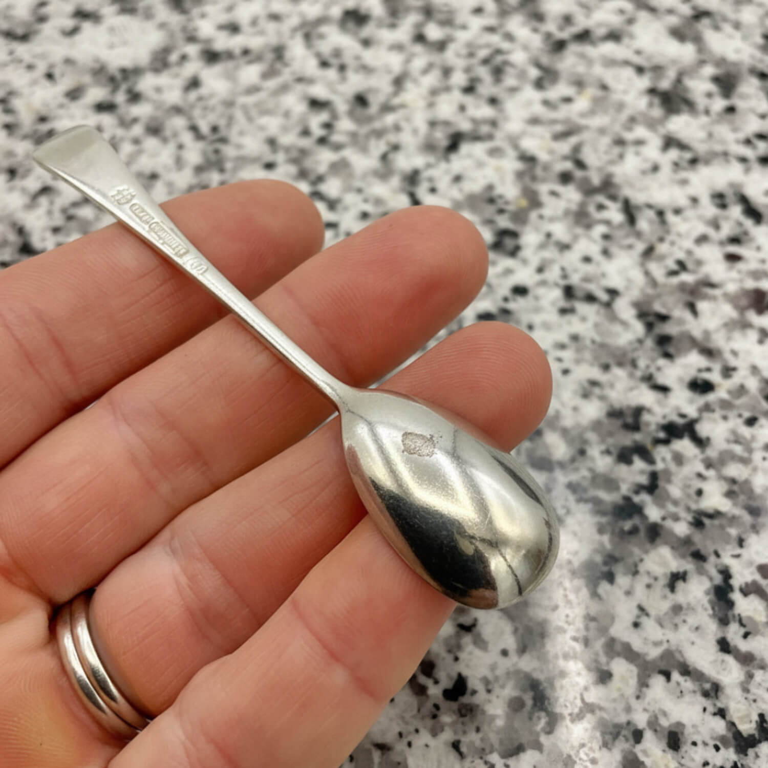 Silver spoon held in a hand against a speckled granite background