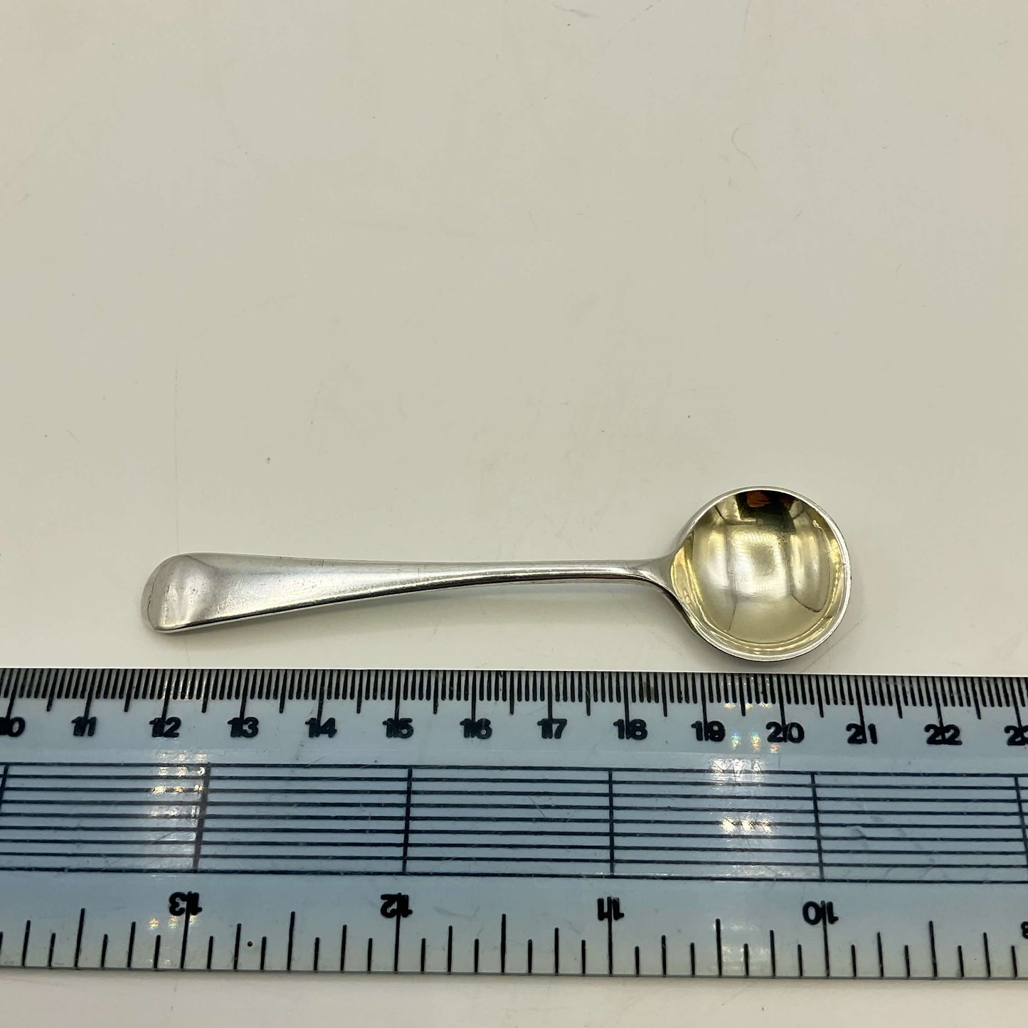 Silver spoon next to a ruler on a white background