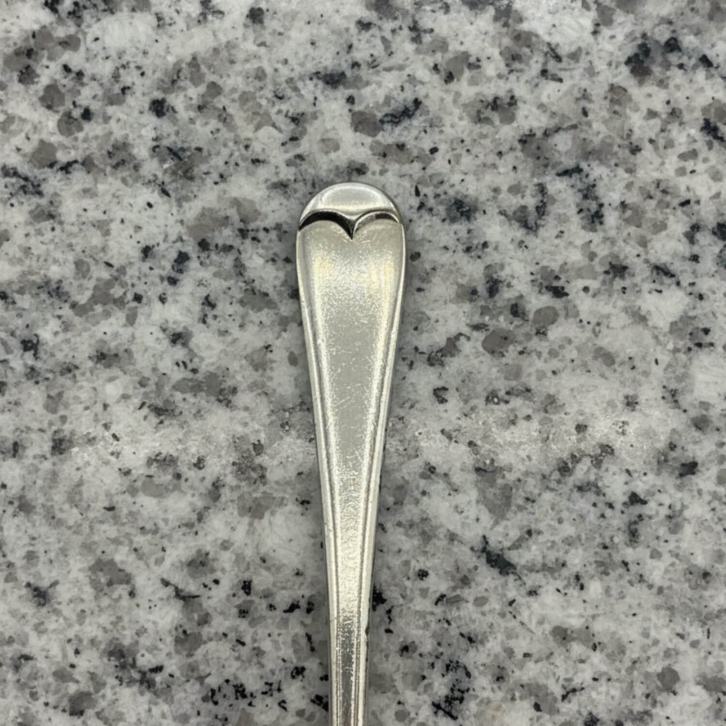 Silver spoon with heart-shaped bowl on a grey granite surface