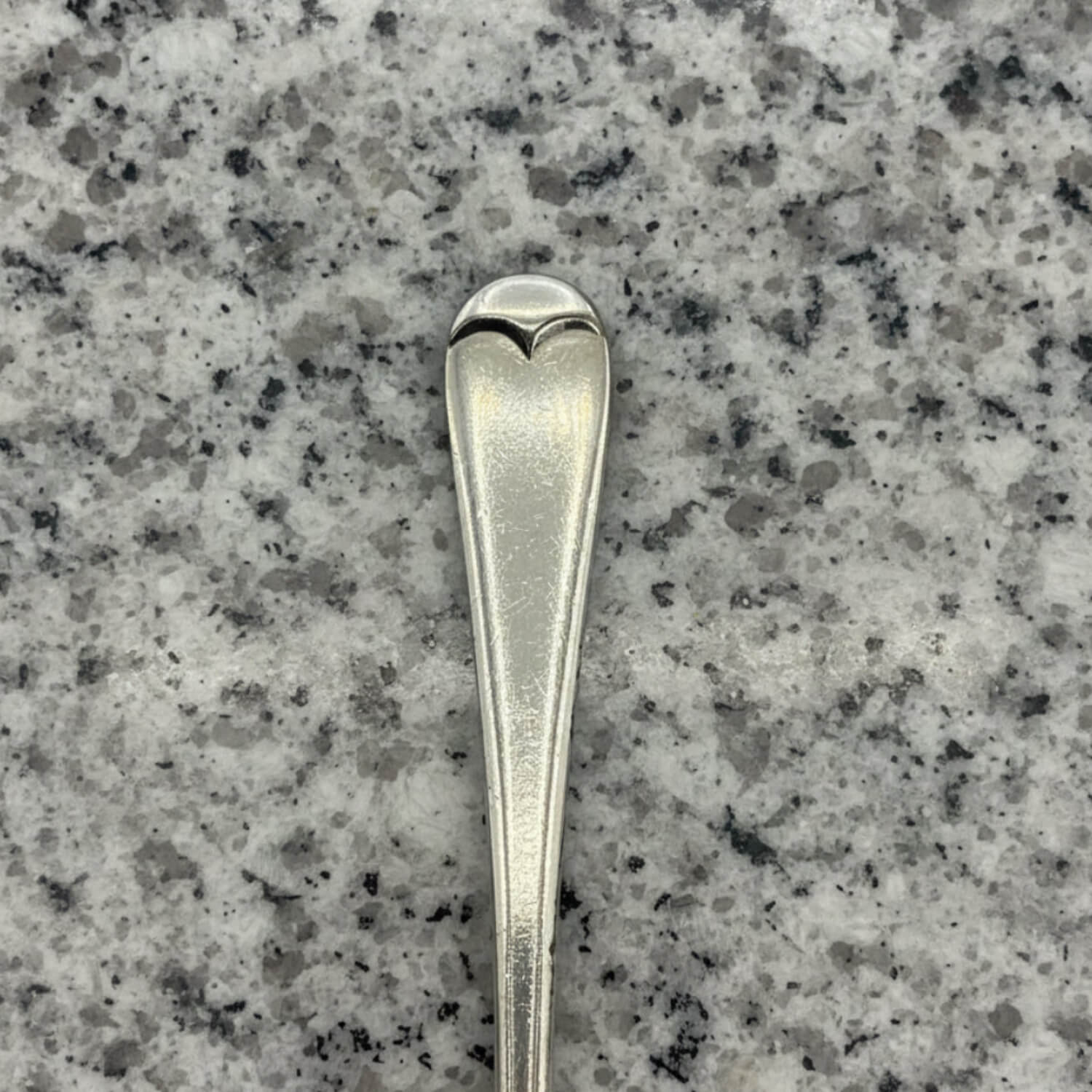 Silver spoon with heart-shaped bowl on a grey granite surface