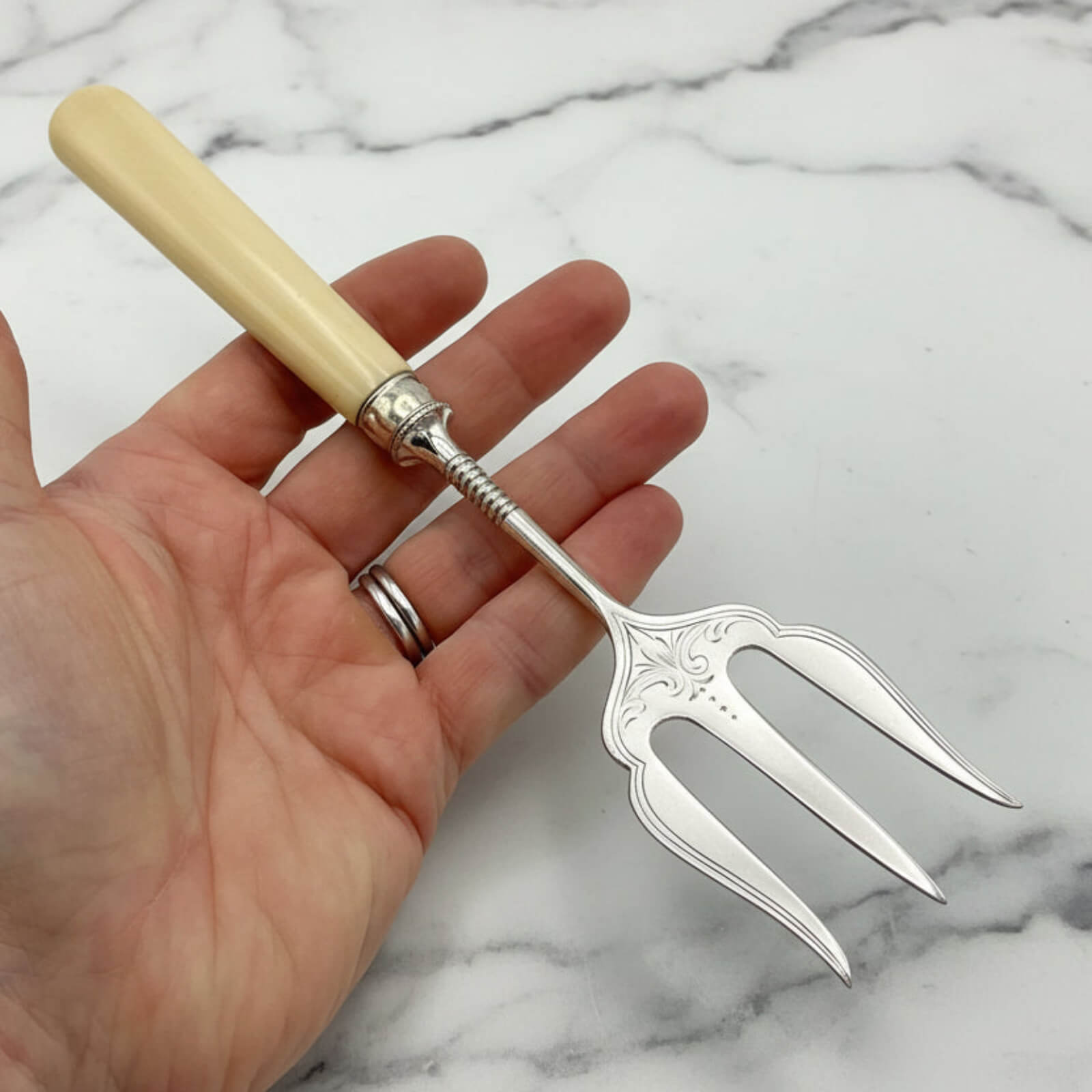 Hand holding a silver fork with a decorative handle on a marble background
