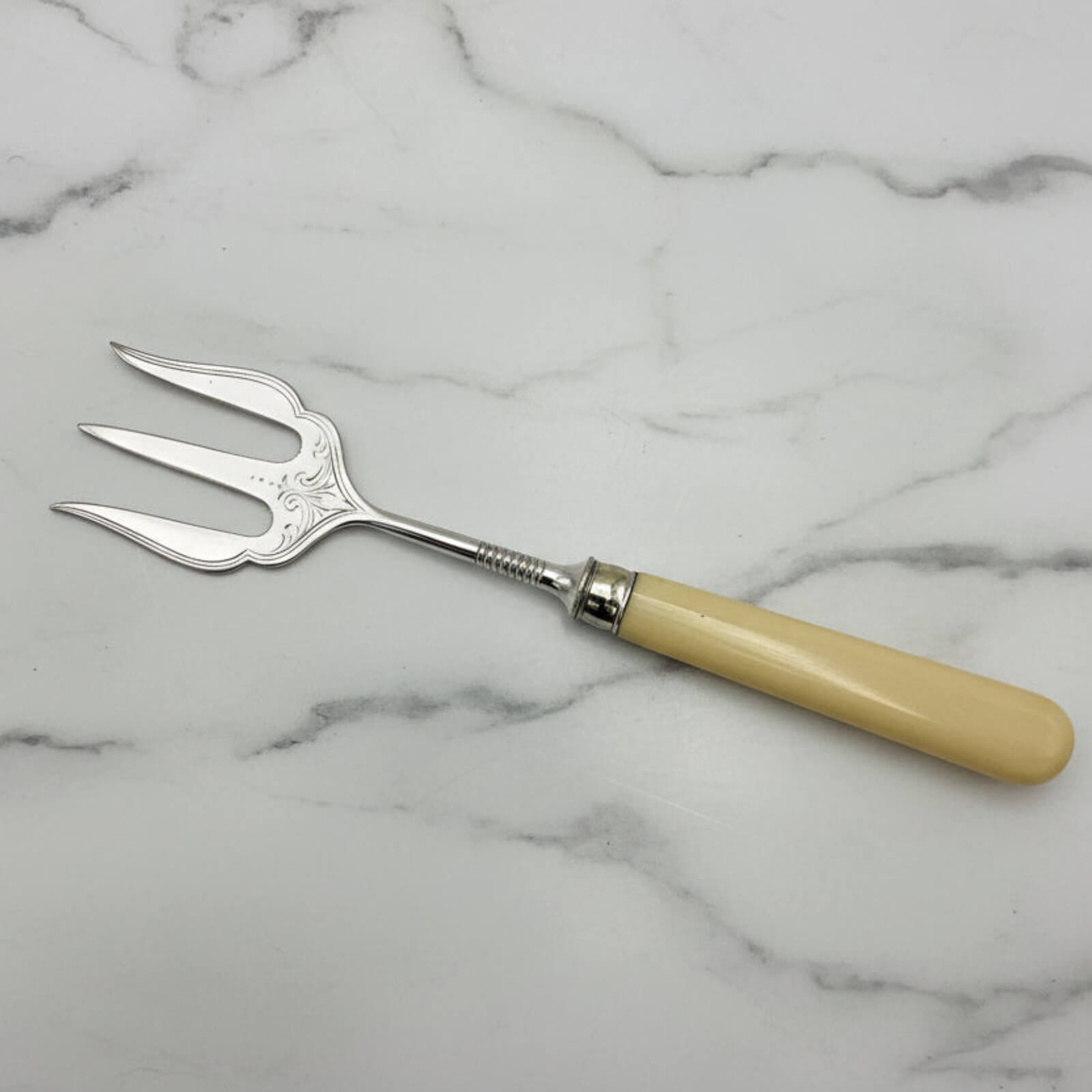 Silver plated fork with a beige handle on a marble surface