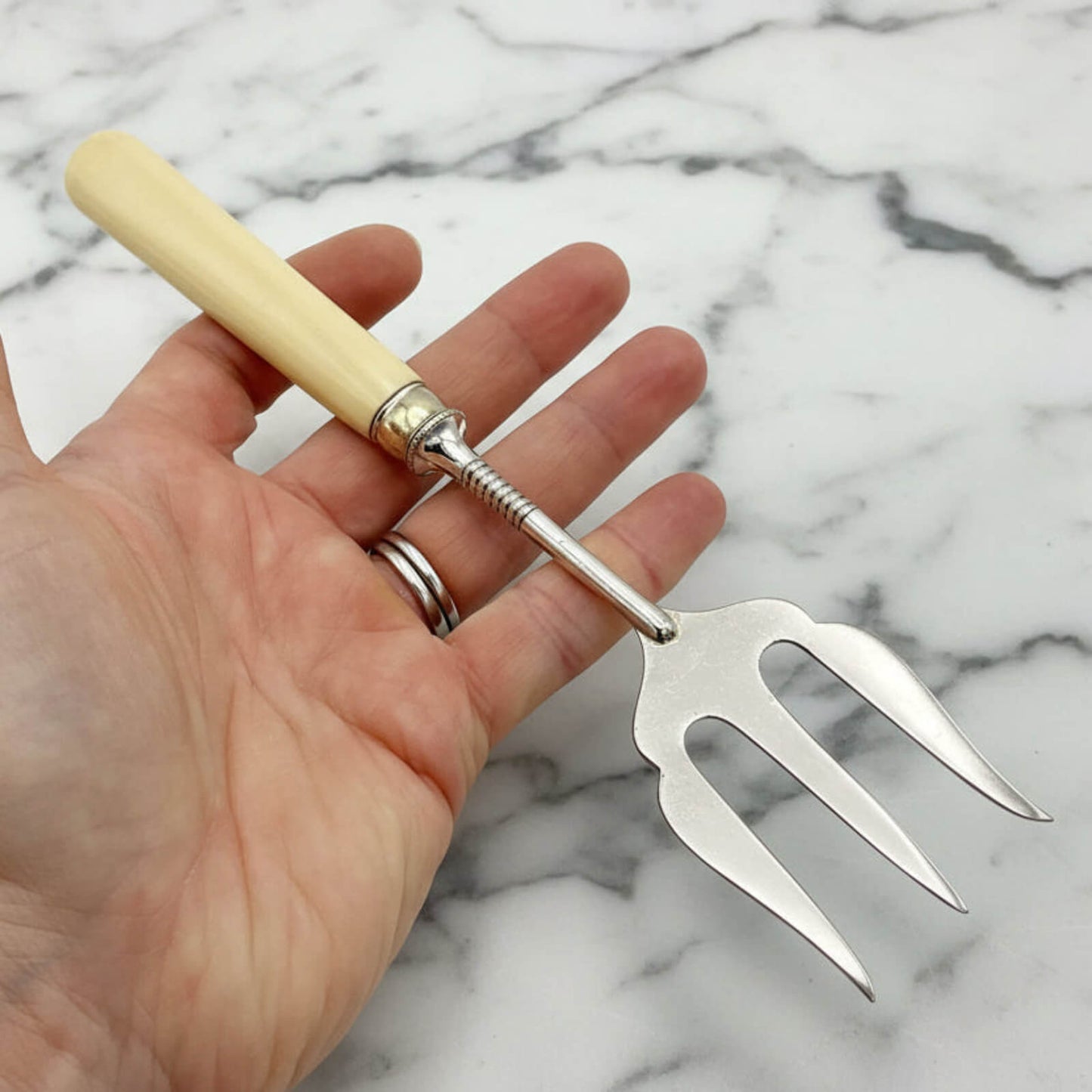 Hand holding a silver fork with a  handle on a marble background