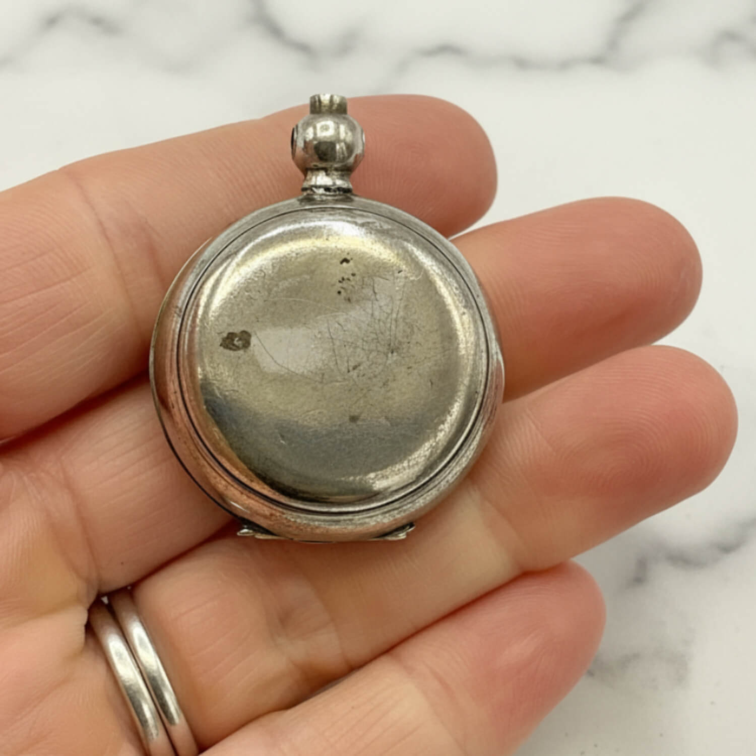 Antique Silver Plated Sovereign Case held in a hand with a marble background