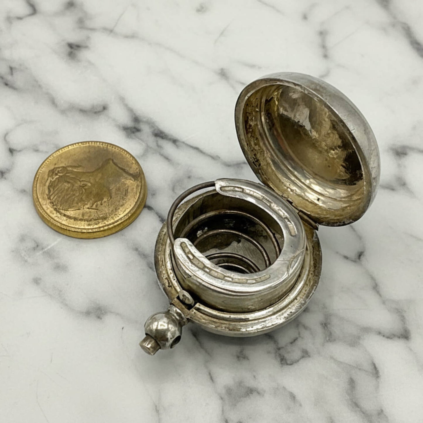 Antique Silver Plated Sovereign Case with lid on a marble surface, next to a gold coloured coin.