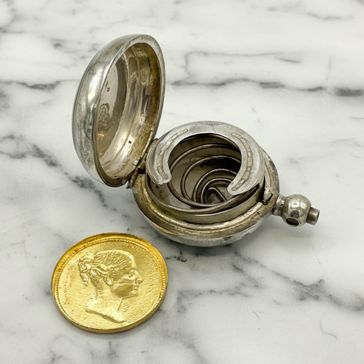 Antique Silver Plated Sovereign Case with open lid on a marble surface, accompanied by a gold coloured coin.