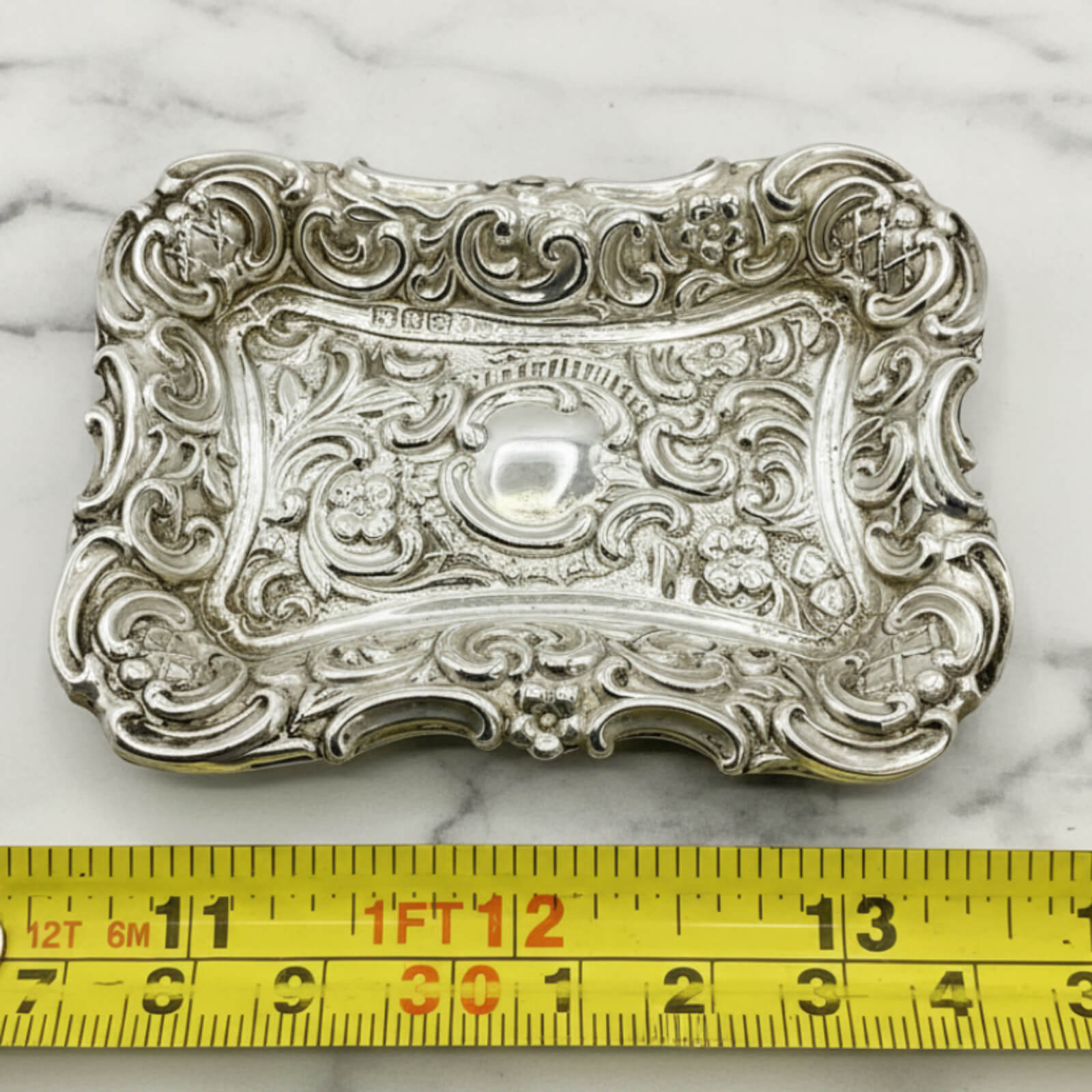 Antique Small Repousse Silver Tray next to a tape measure for scale on a marble surface