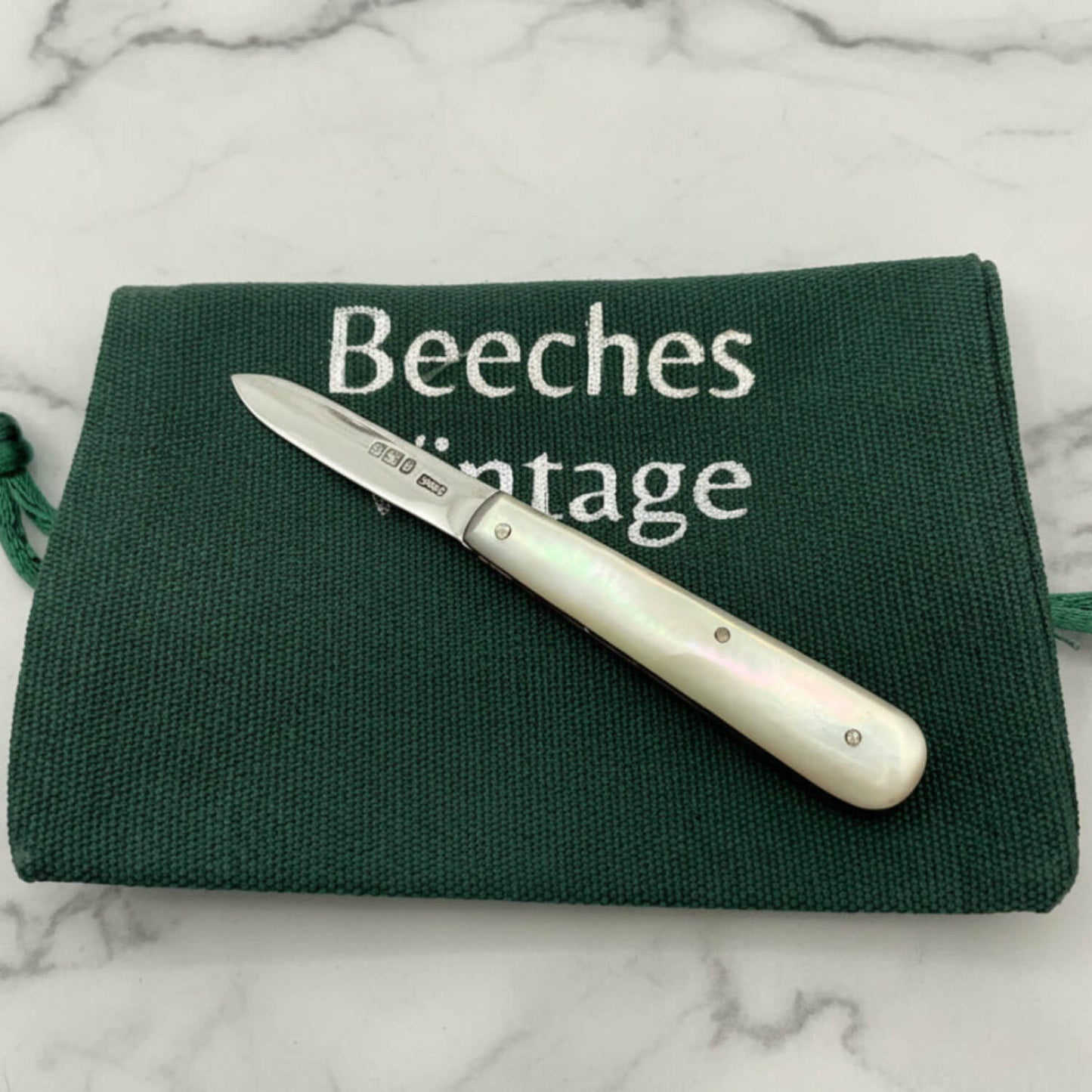 Fruit Knife with a pearl handle on a green cloth bag labeled 'Beeches Vintage' on a marble surface