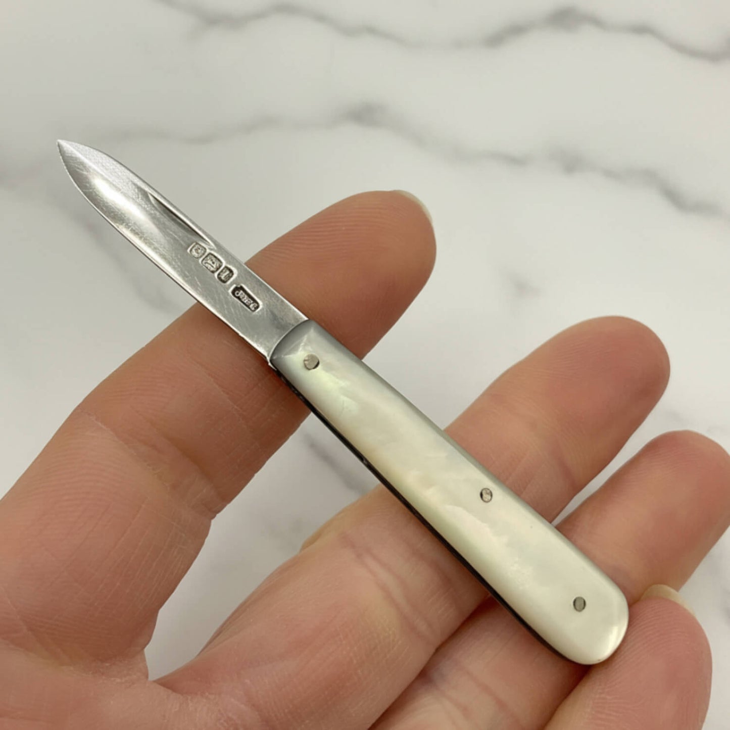 Hand holding a small fruit knife with a white pearl handle and silver blade