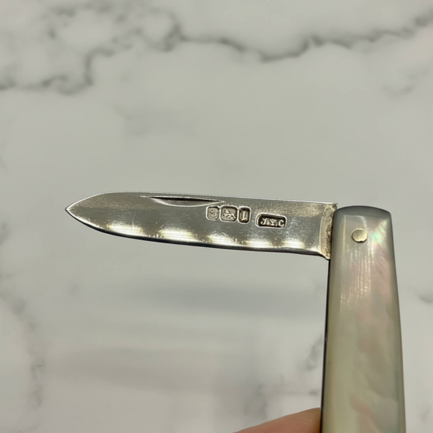 Silver fruit knife with engraved details on a marble background