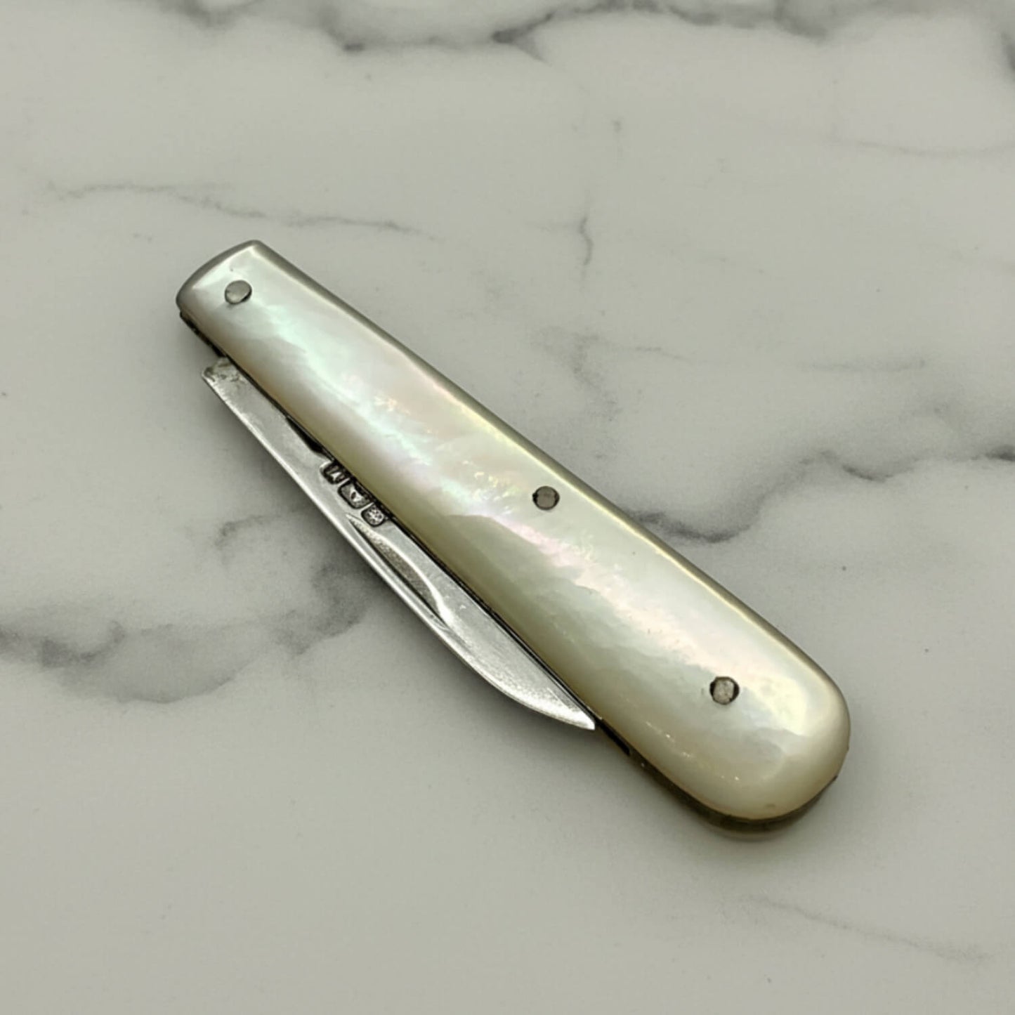 Silver fruit knife with a pearl handle on a marble surface