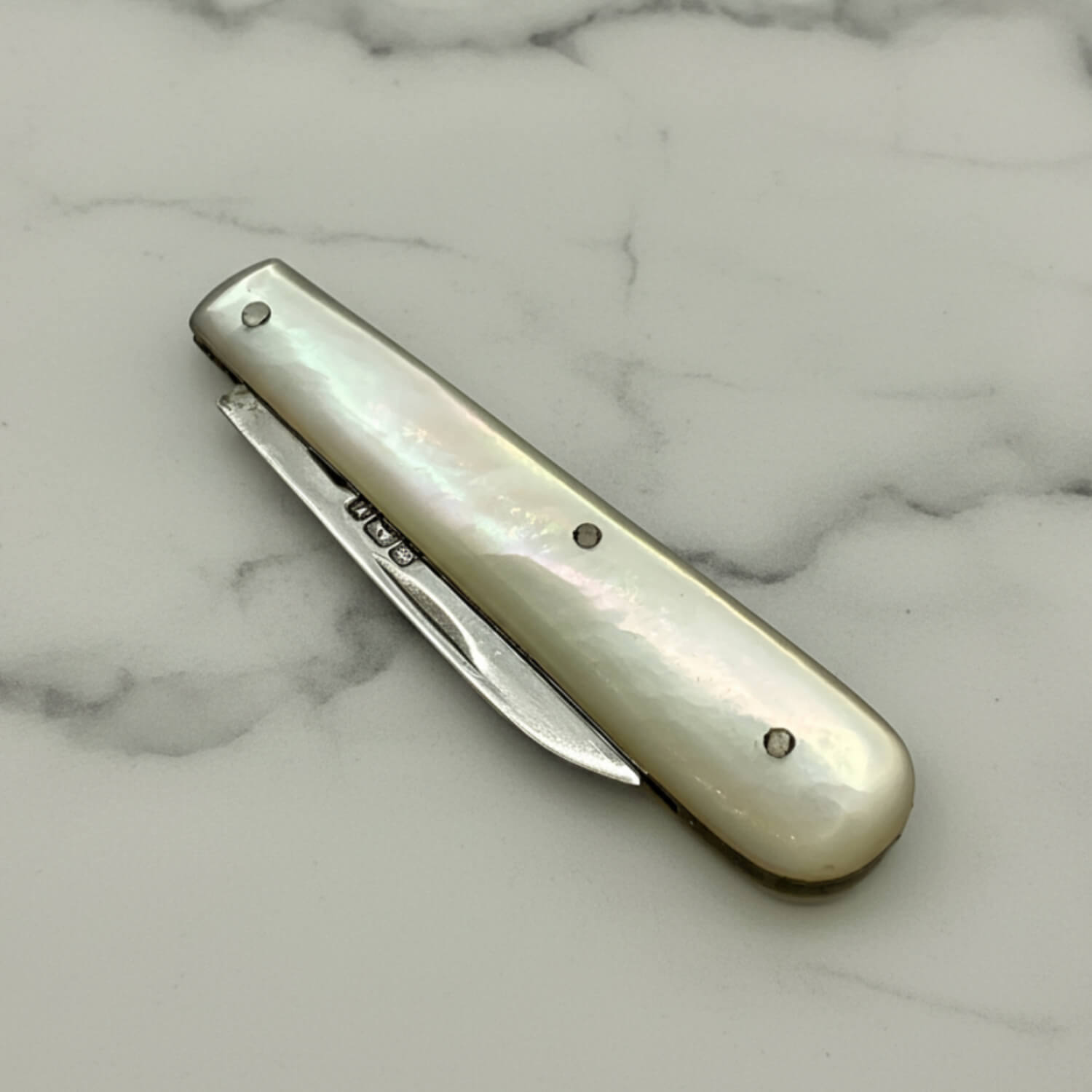 Silver fruit knife with a pearl handle on a marble surface