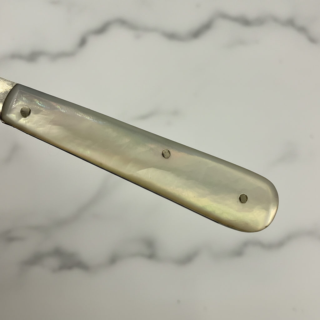 Silver fruit knife handle with a mother of pearl handle on a marble surface