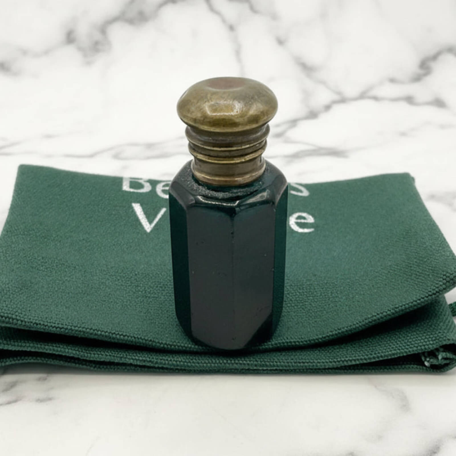 Blue glass bottle with brass cap on green fabric with visible text, against a marble background