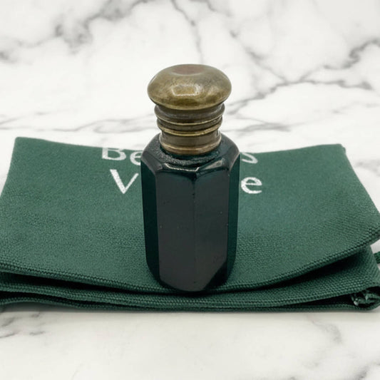Blue glass bottle with brass cap on green fabric with visible text, against a marble background