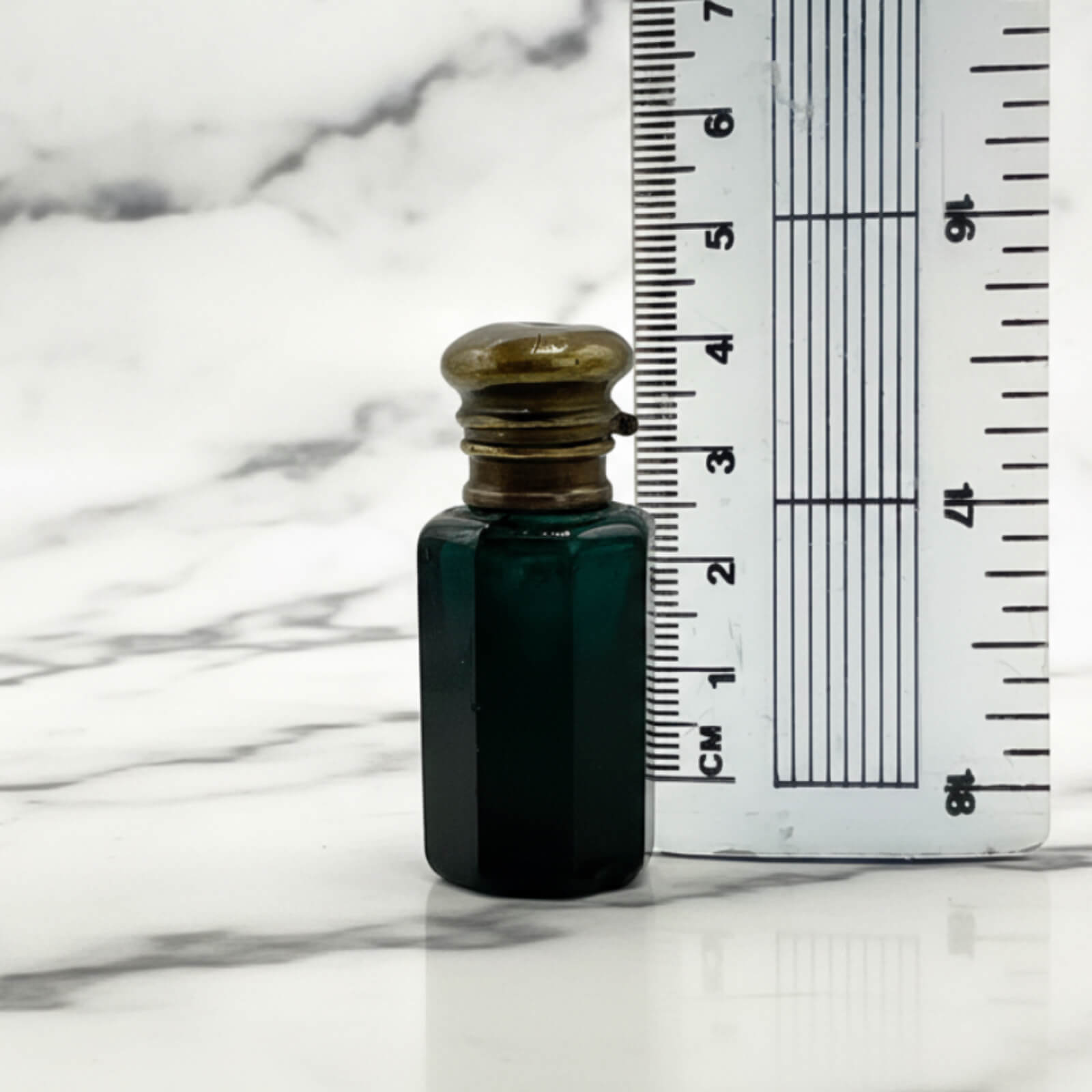 Small blue bottle with a brass cap next to a ruler on a marble surface