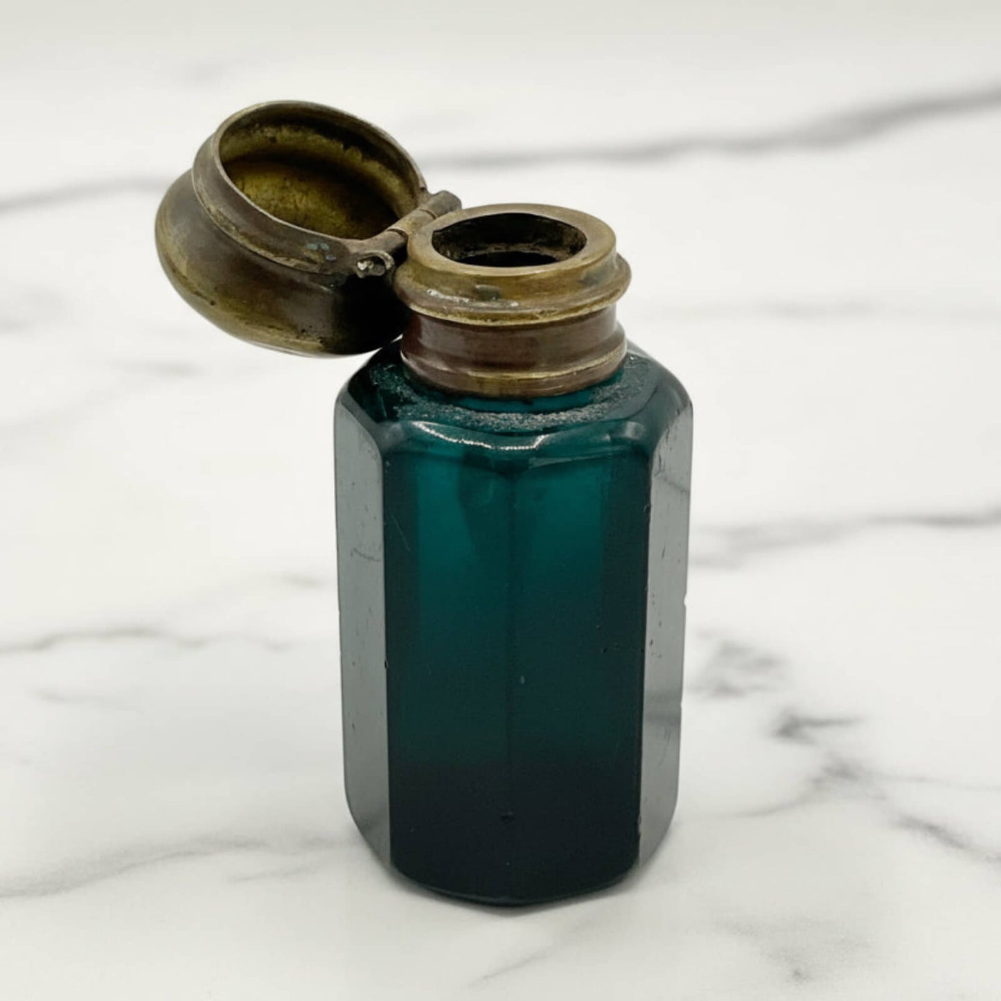 Vintage blue glass bottle with brass cap on a marble surface