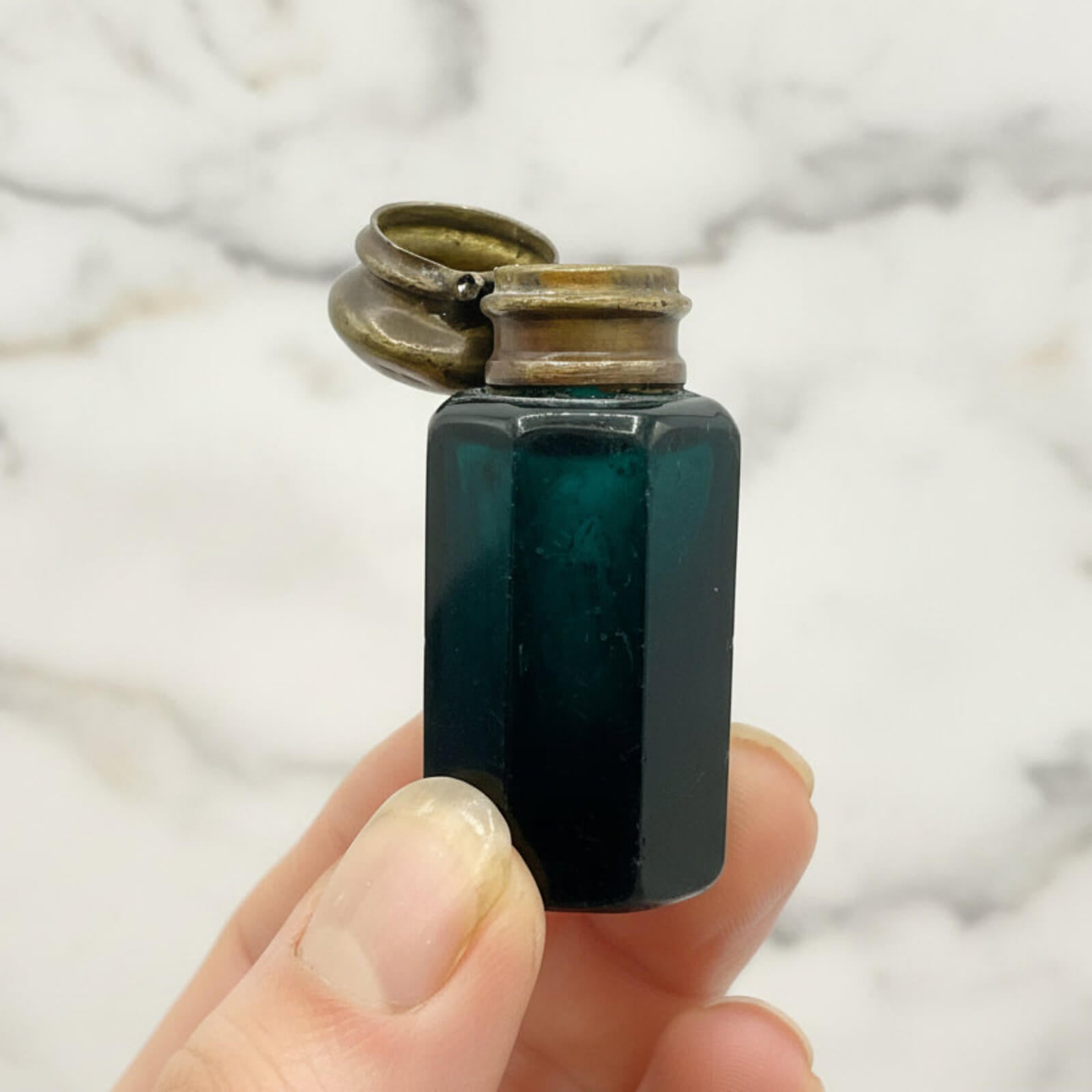 Small blue glass bottle with a metal cap held in a hand against a neutral background