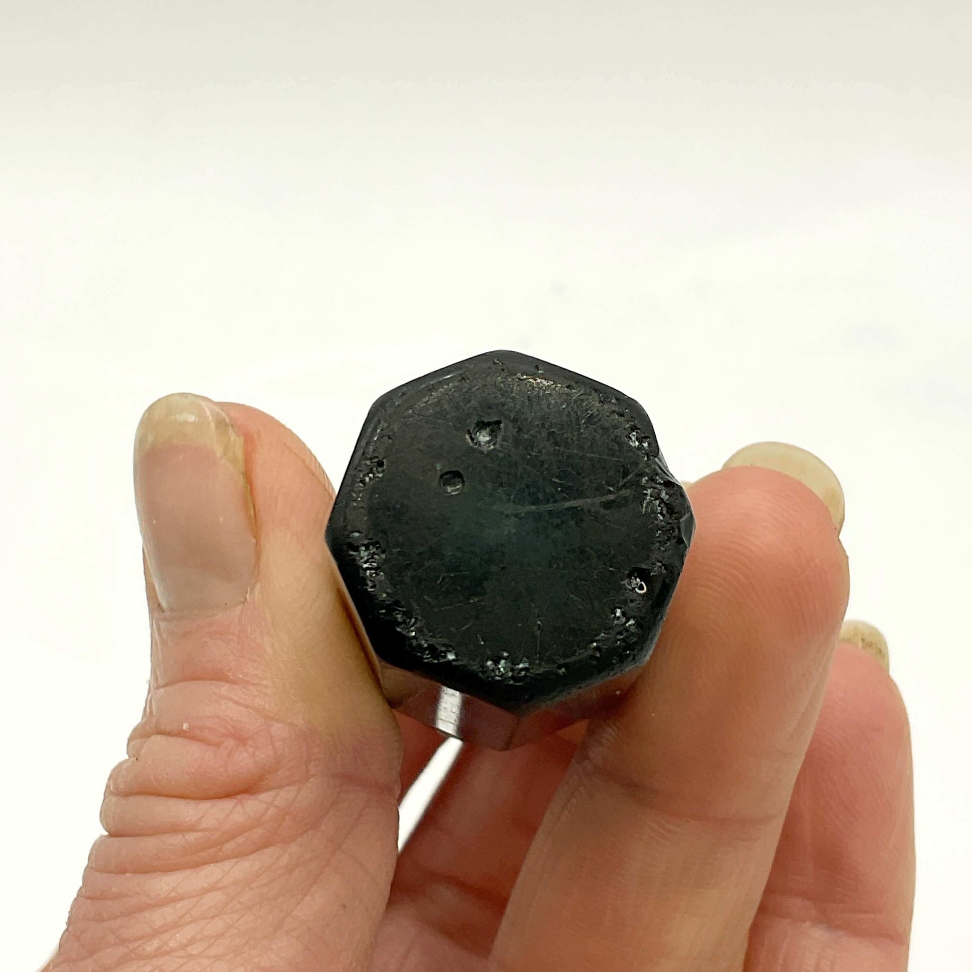 base of glass bottle held between fingers against a white background