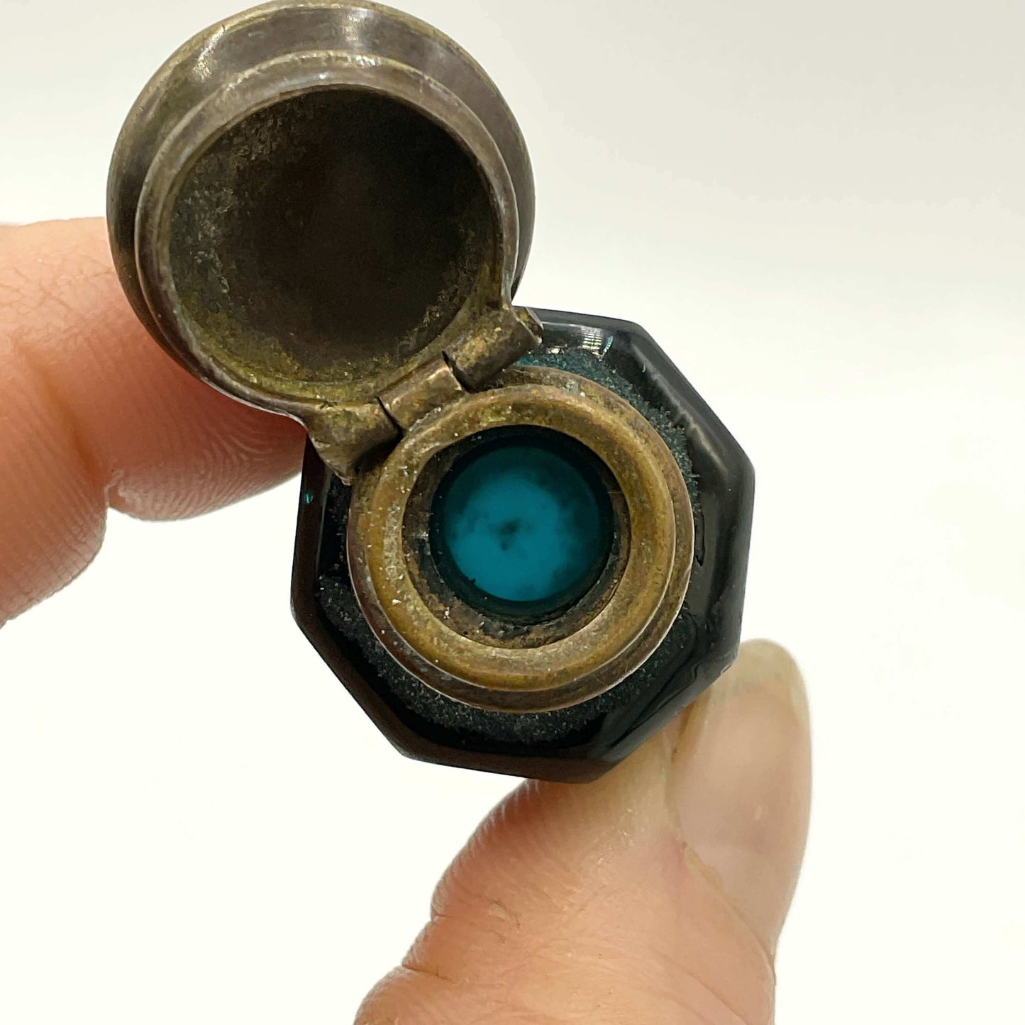 Close-up of a small glass bottle held between fingers against a white background