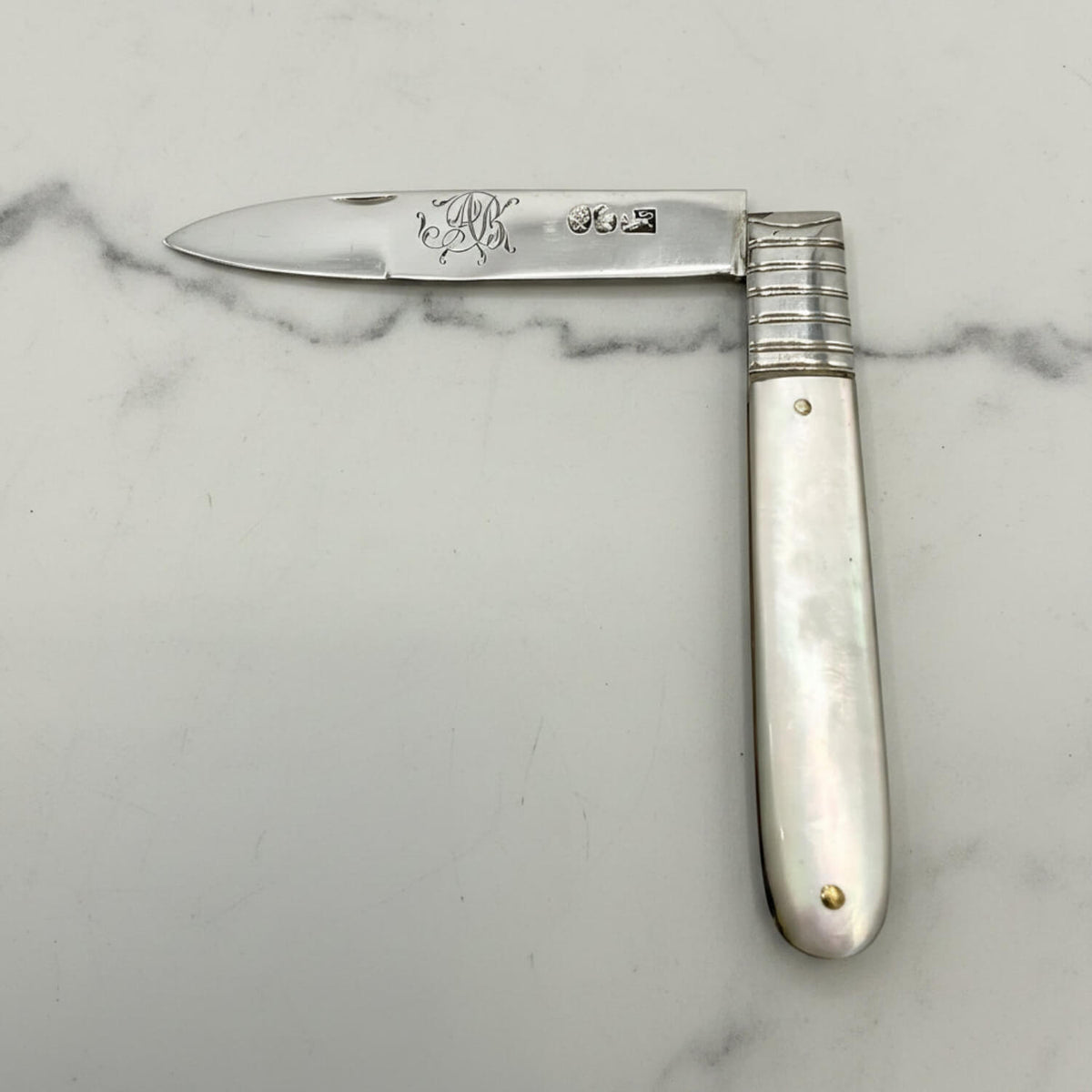 Antique  silver fruit knife with a silver blade and mother of pearl handle, featuring engraved initials and a ribbed metal bolster, displayed on a light gray background.