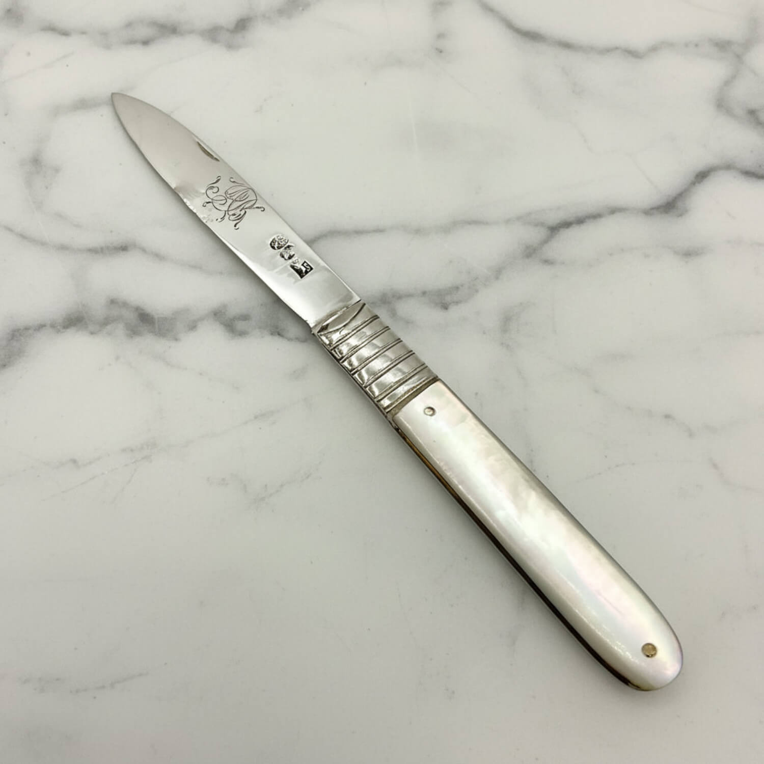 An silver fruit knife with a silver blade and handle, featuring a mother-of-pearl inlay and a textured grip, shown on a neutral light gray background.