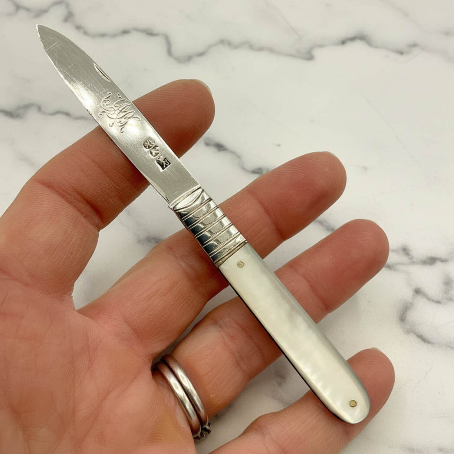 Antique silver knife with an engraved blade and a mother of pearl handle, held in a person's hand against a plain white background.